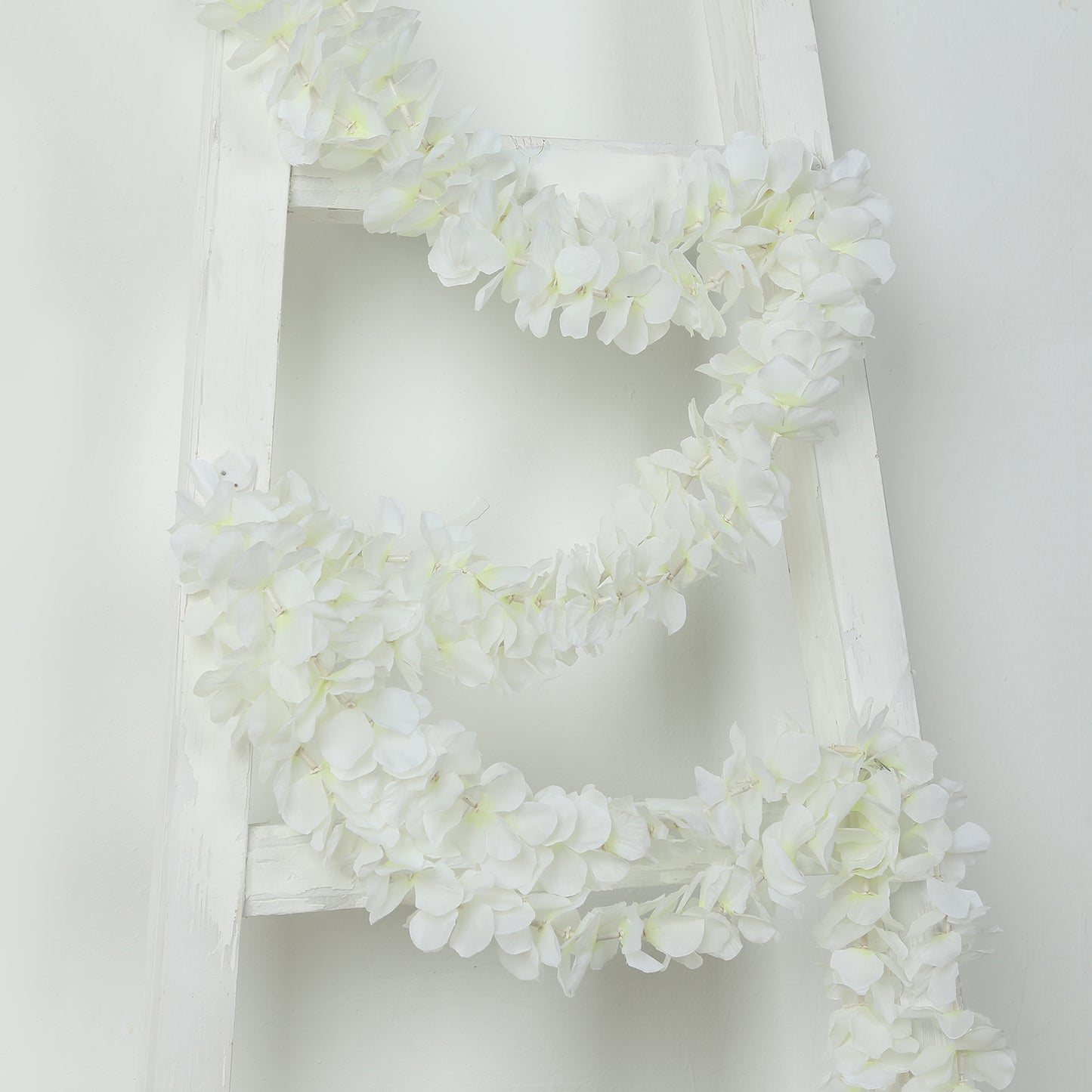 White artificial wisteria vine garlands on a white ladder.