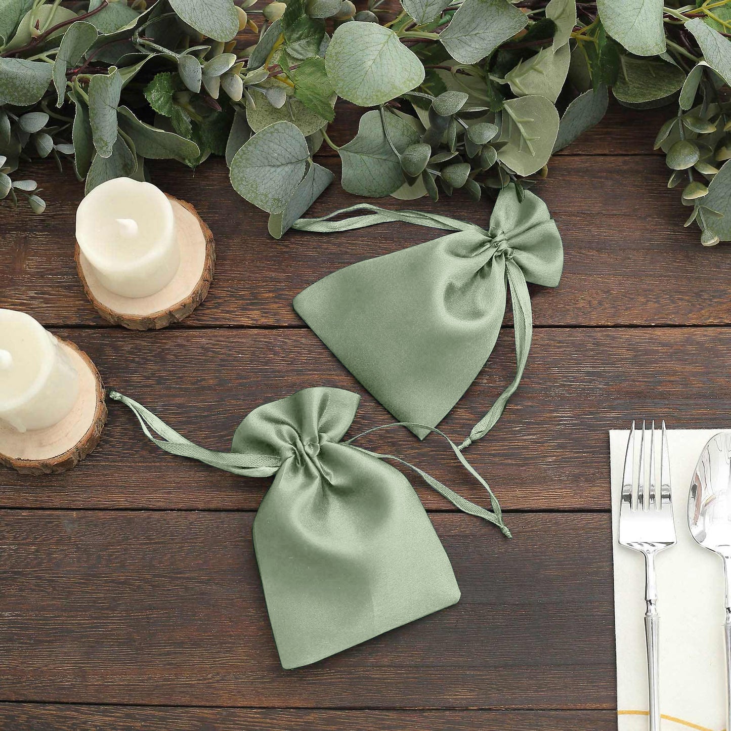 Sage green satin drawstring wedding favor bags on a wooden table.