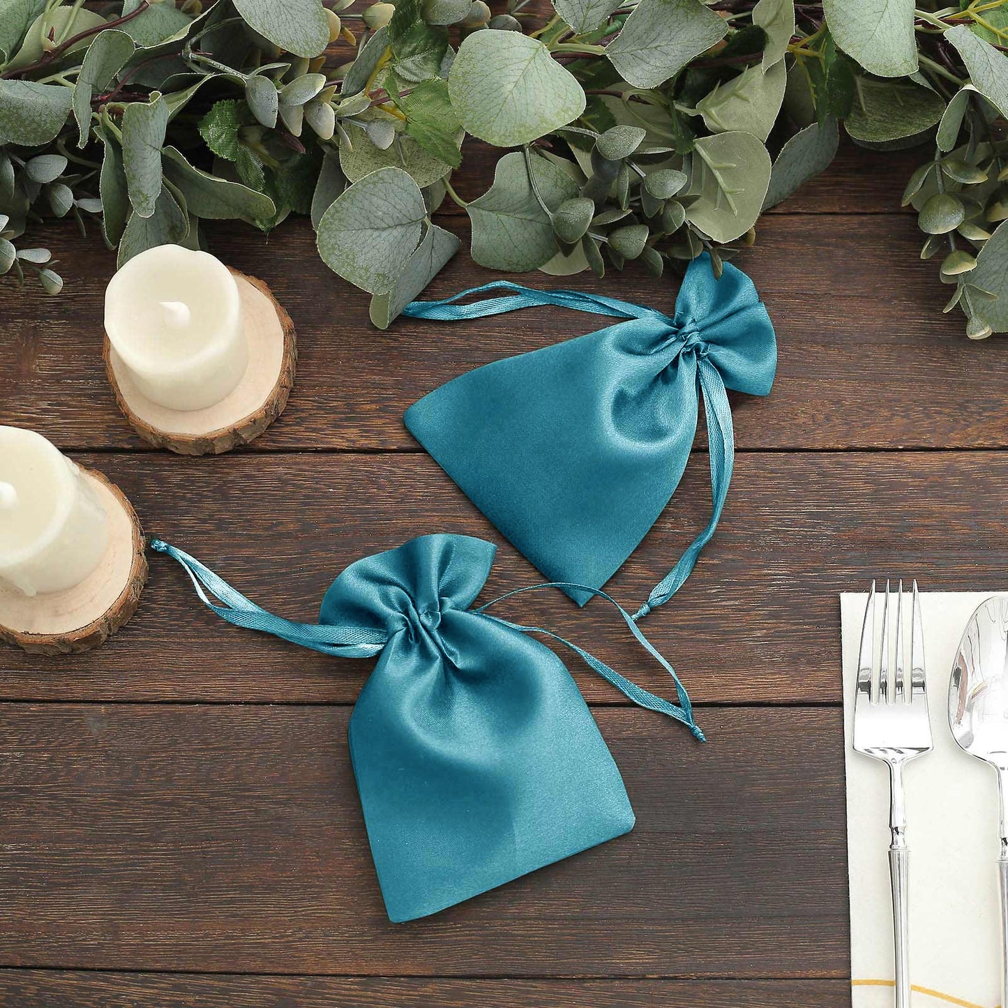 Turquoise satin drawstring favor bags on a wooden table with greenery.