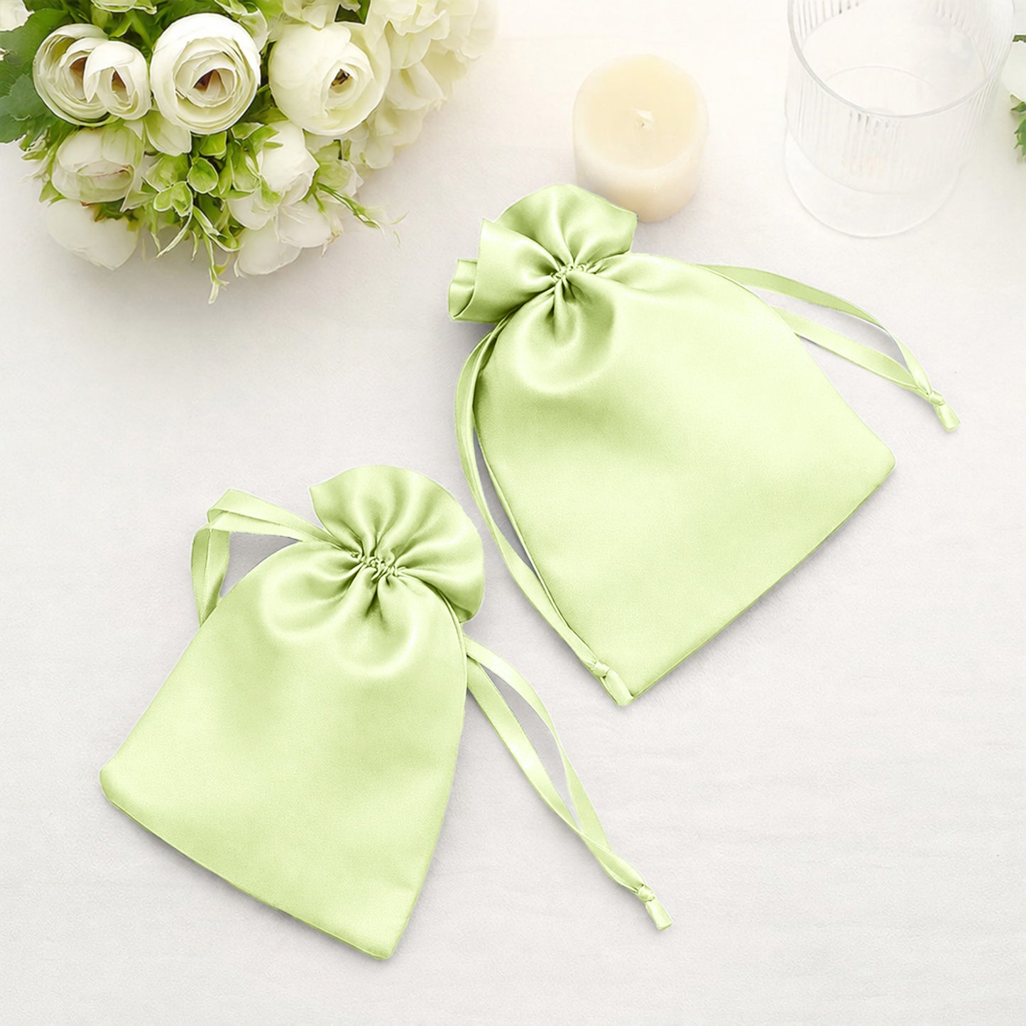 Apple green satin drawstring wedding favor gift bags on a table.