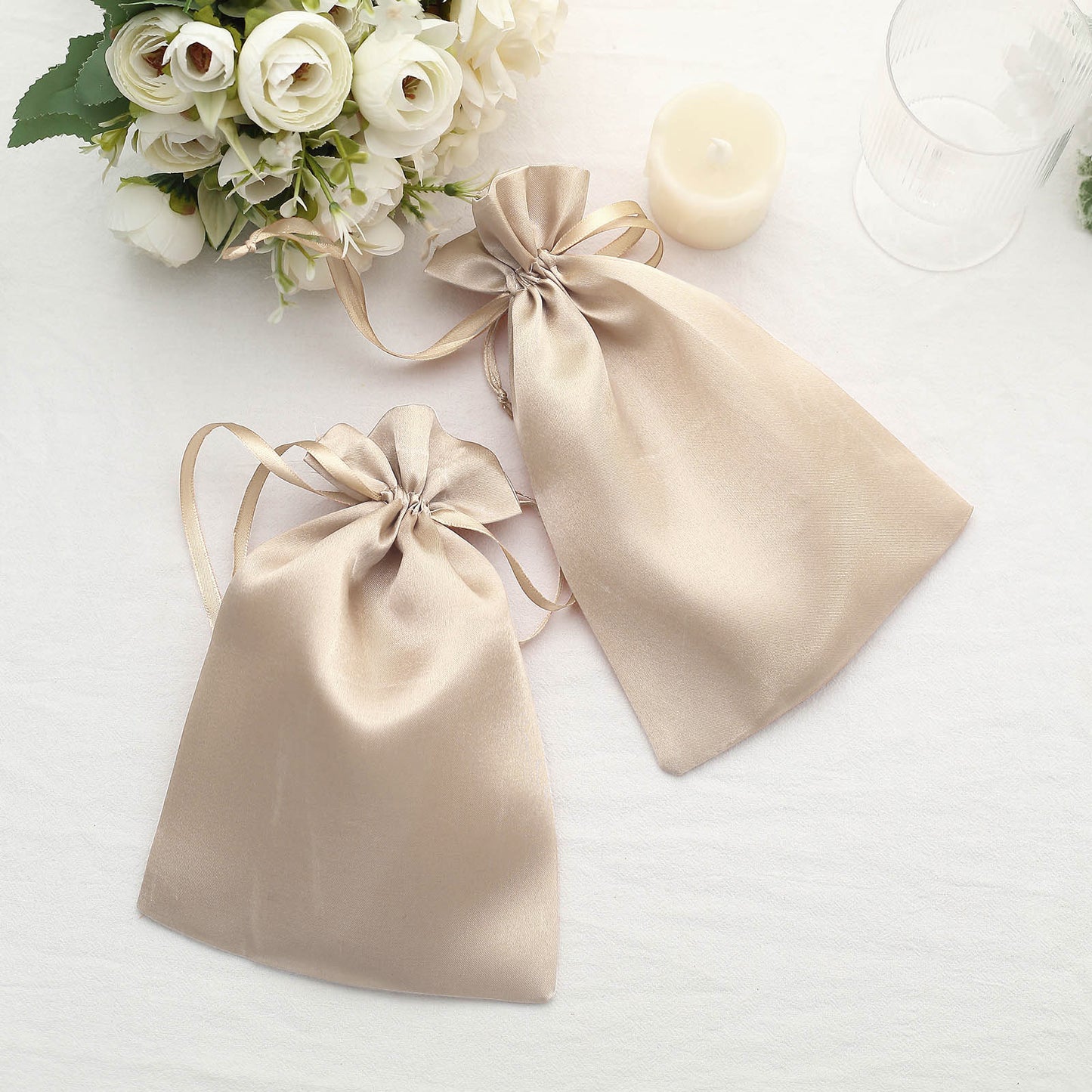 Beige satin drawstring wedding favor bags on a table.