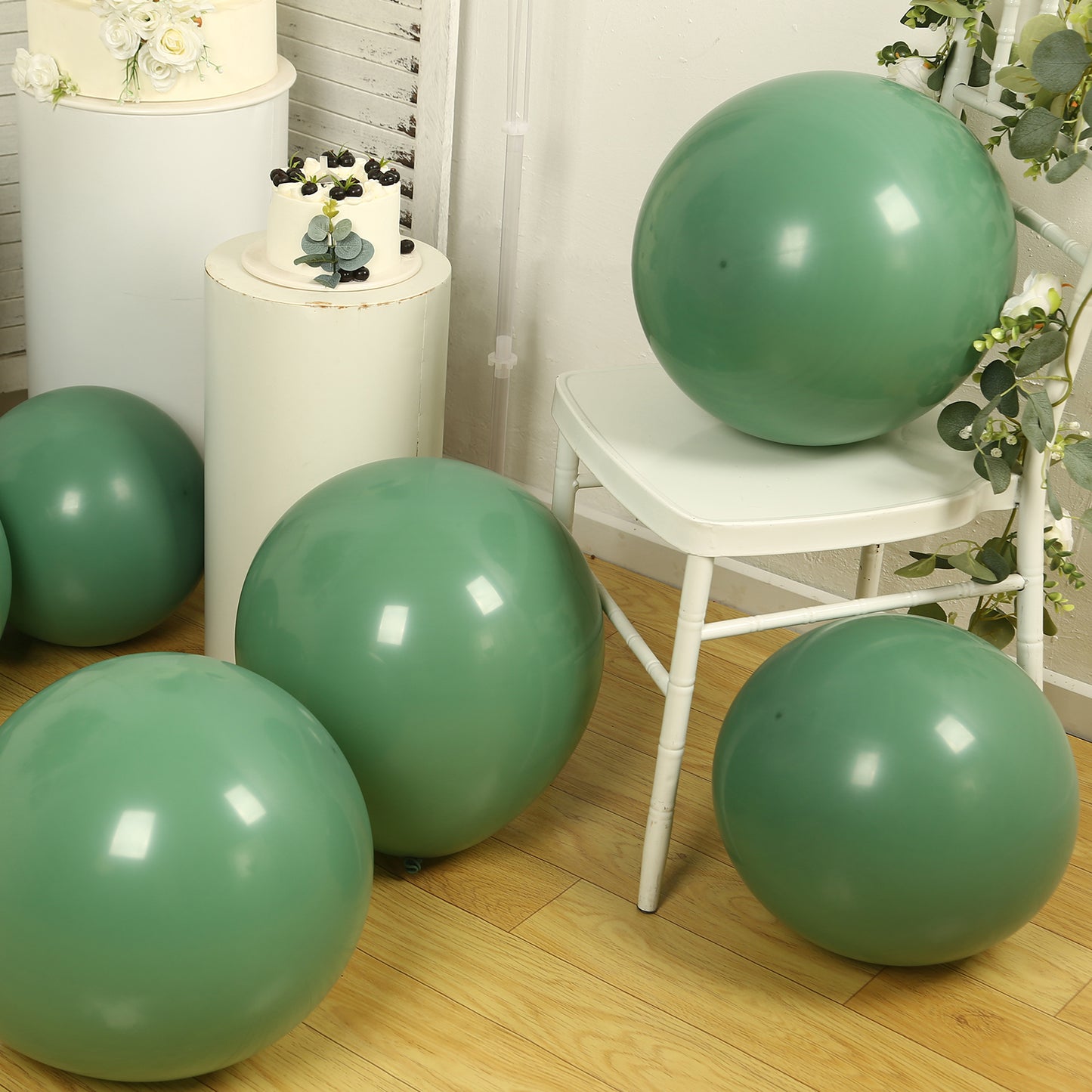 Matte pastel dusty sage green biodegradable balloons on a wooden floor.