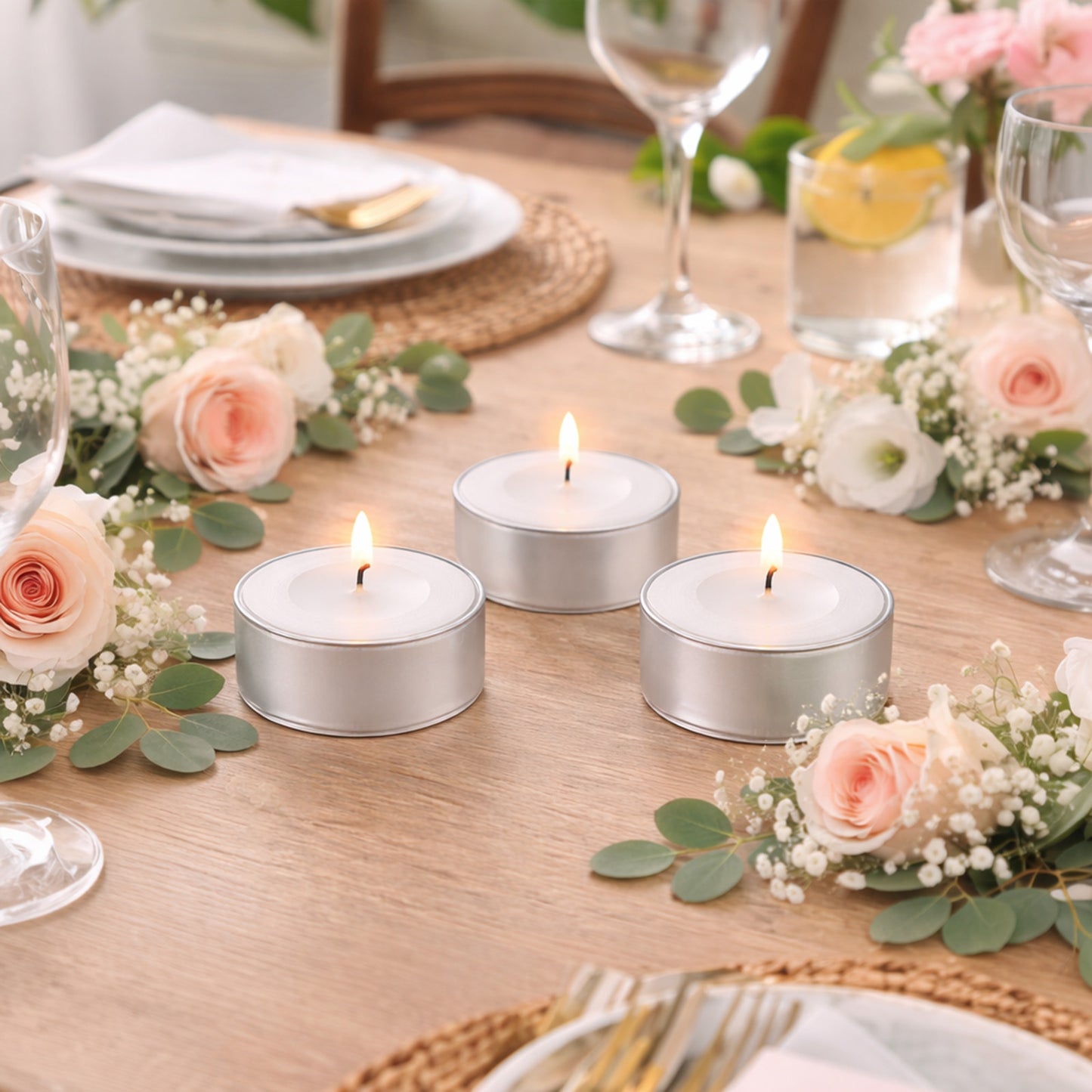 White tealight candles in metal cups on a table with flowers.