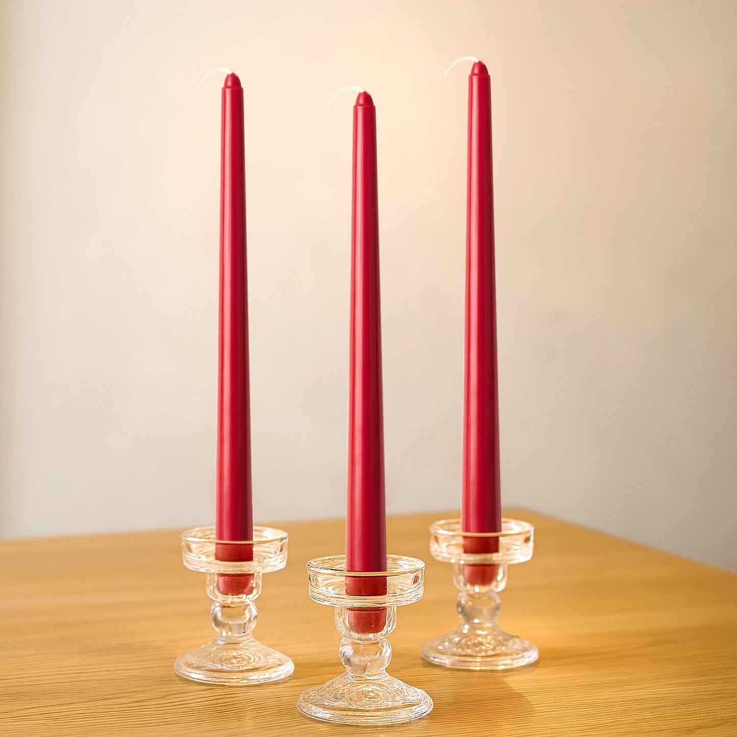 Red premium wax taper candles in glass holders on a wooden table.