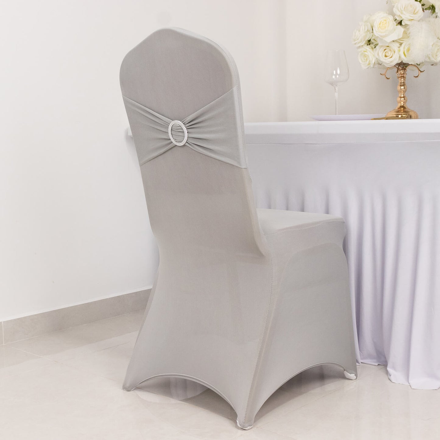 Silver spandex banquet chair cover with rhinestone buckle on a fitted chair.