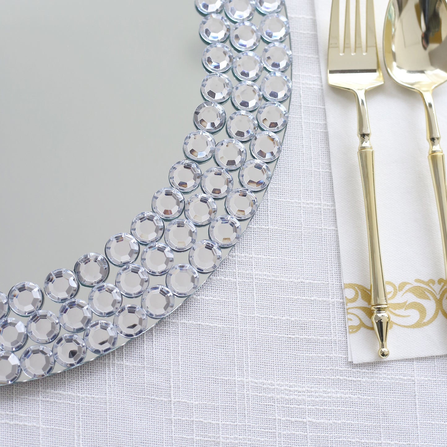 Silver charger plates with diamond beaded rim on a white table setting.