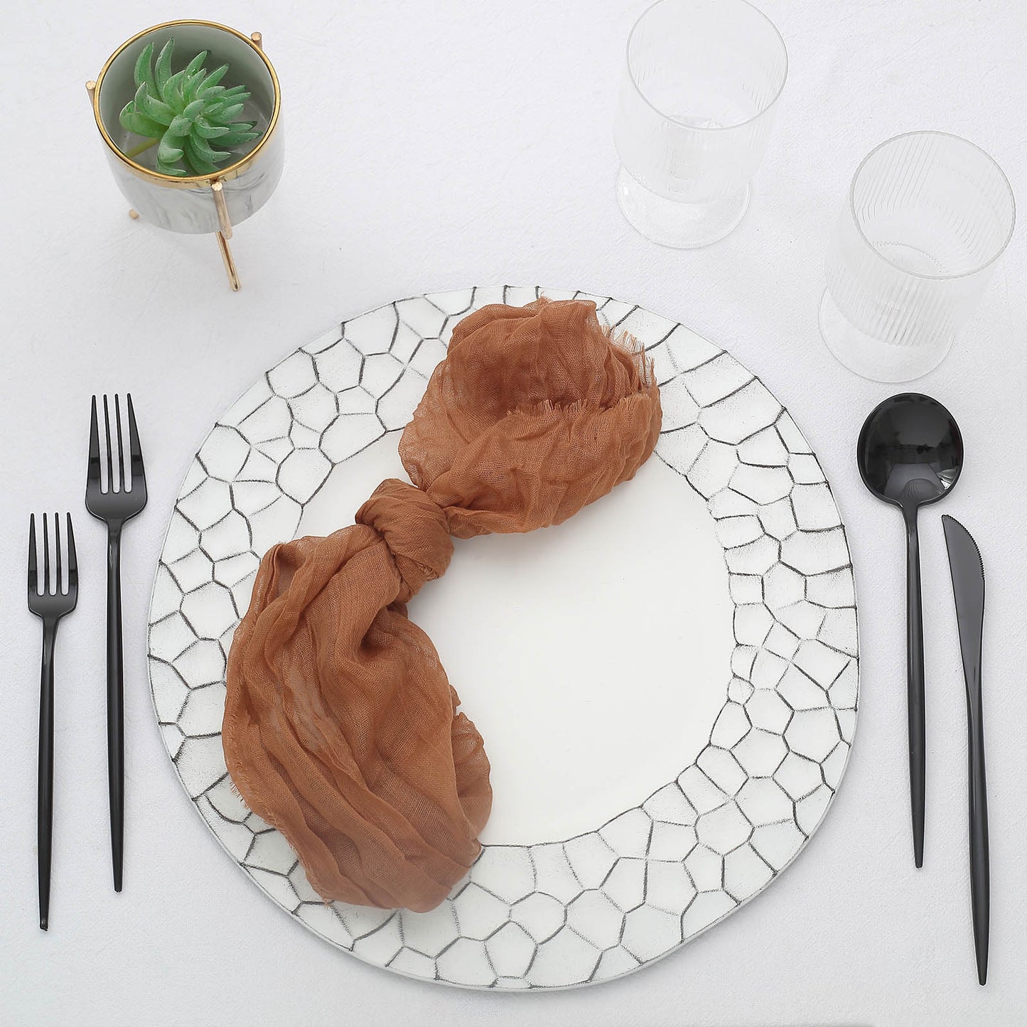Elegant white plate setting with brown scarf napkin and black cutlery.