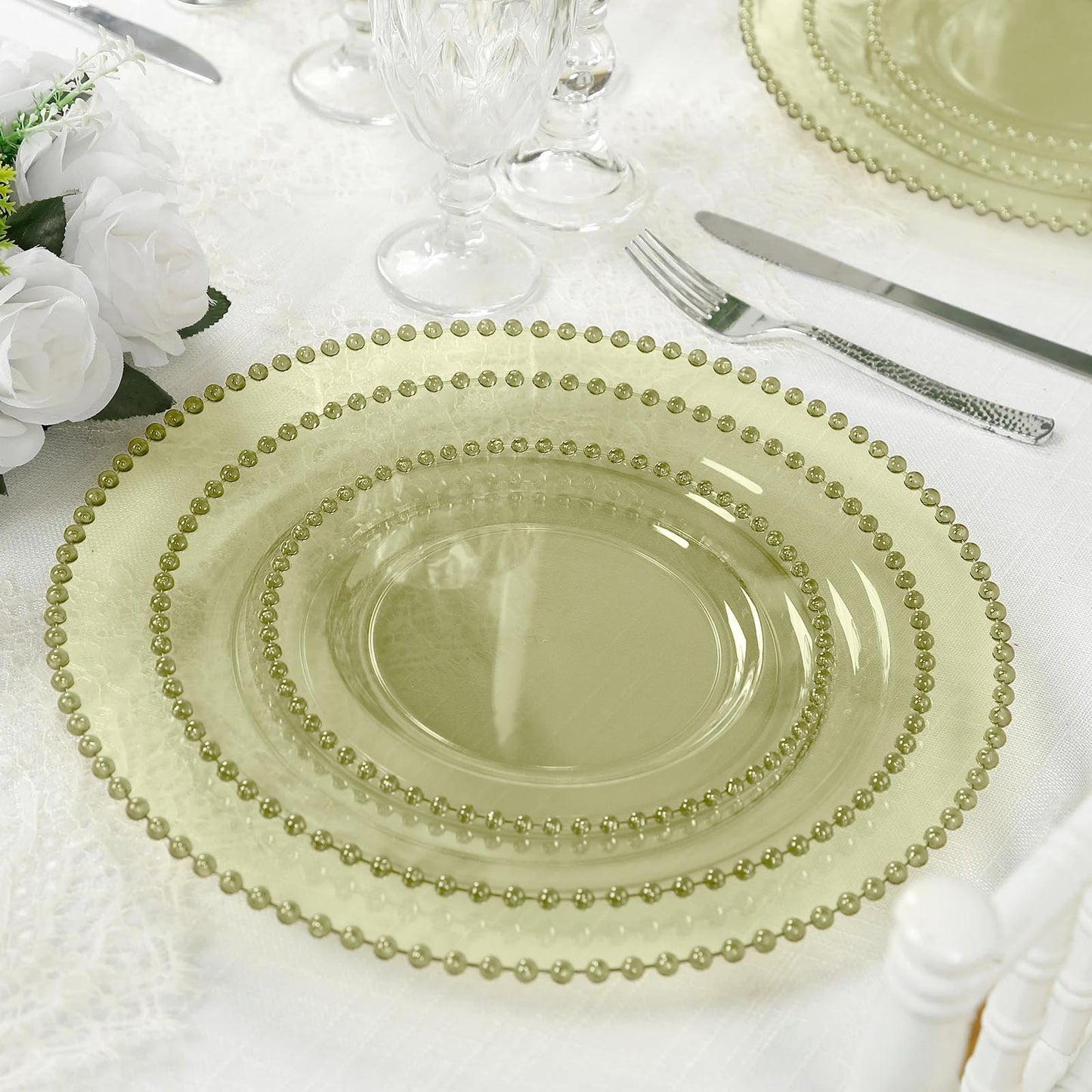 Transparent dusty sage green charger plates with beaded rim on a dining table.