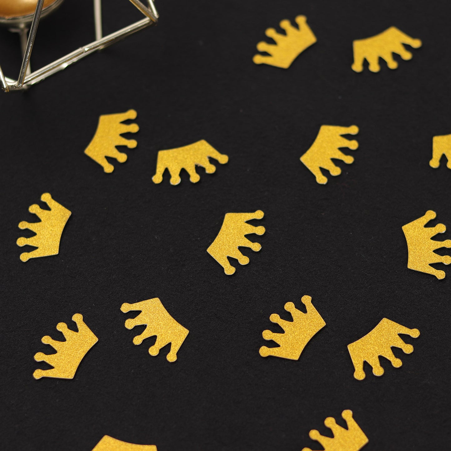 Gold glitter crown paper confetti scatters on a black surface.