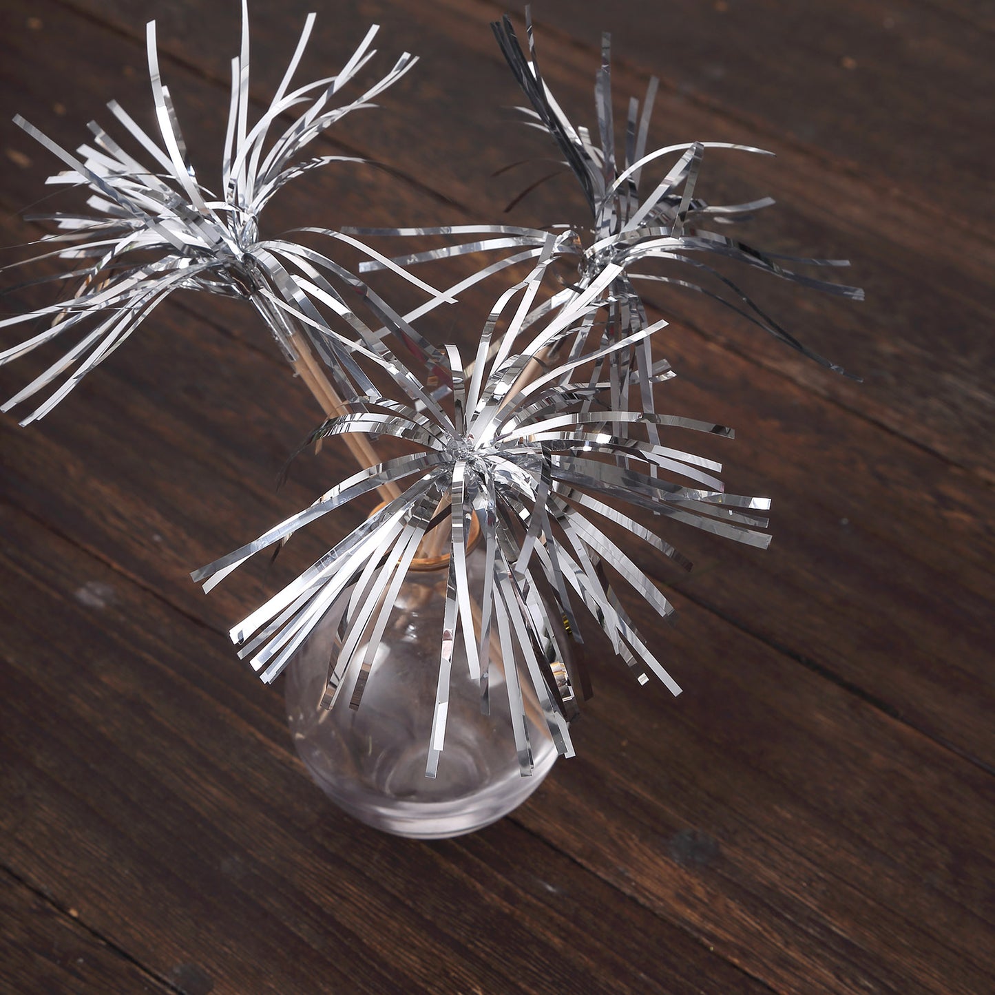 Silver firework frills cake toppers in a clear vase on wooden surface.