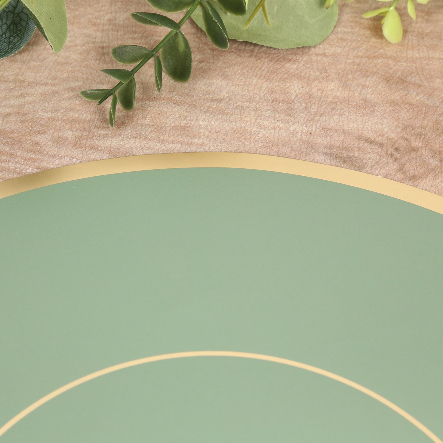 Sage green disposable placemat with gold rim on a textured background.