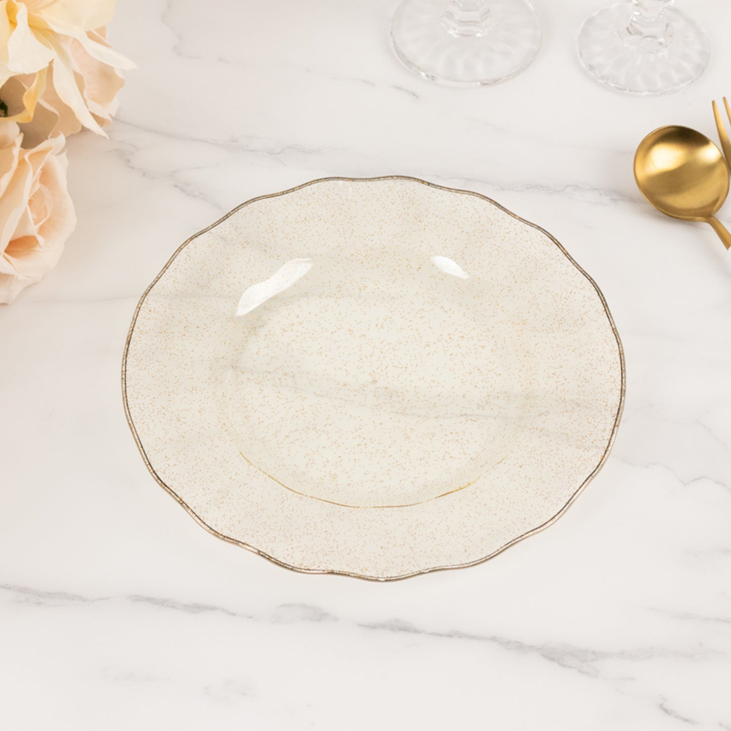 Gold glitter plastic dinner plate with ruffled rim on a marble surface.