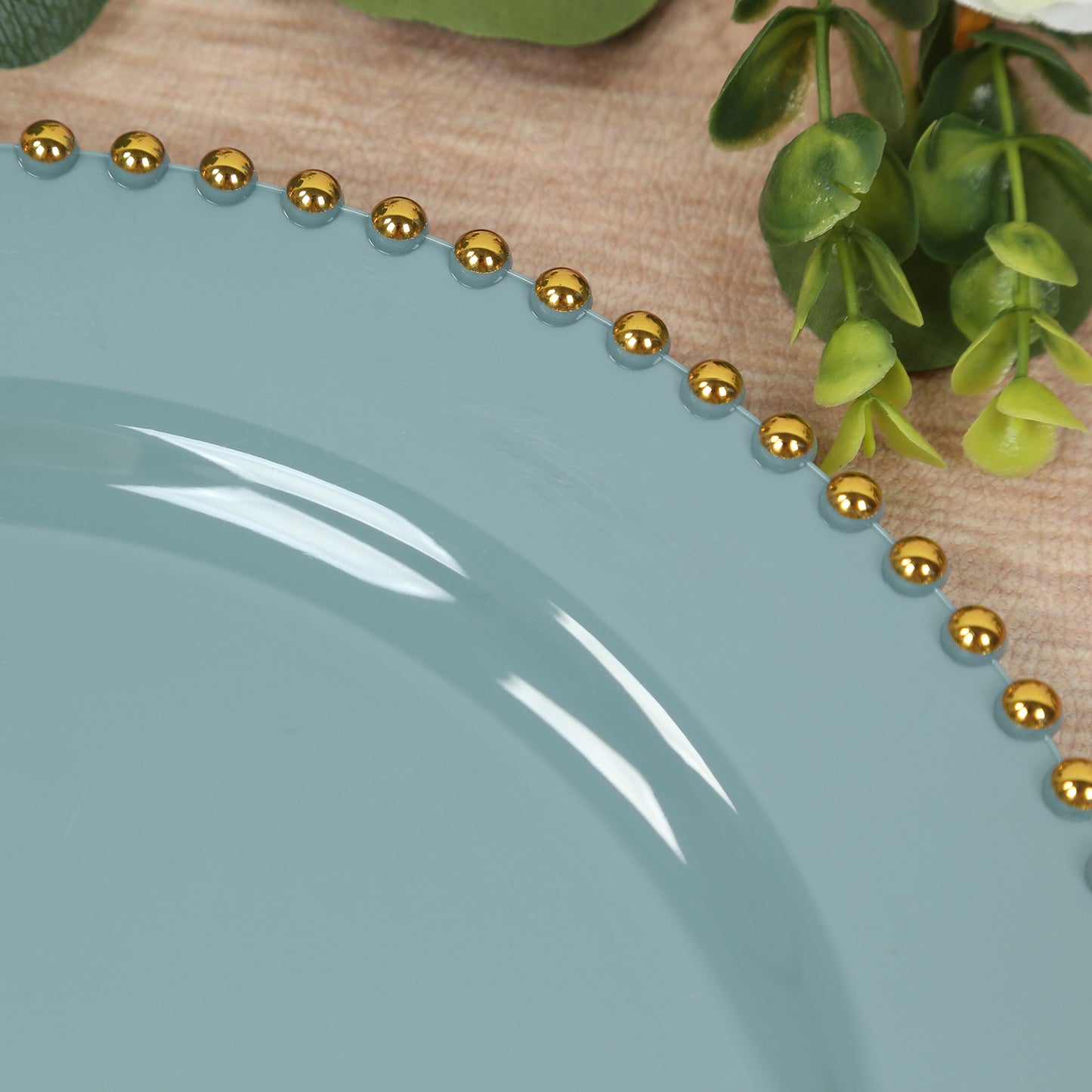 Dusty blue round dinner plate with gold beaded rim on a wooden surface.