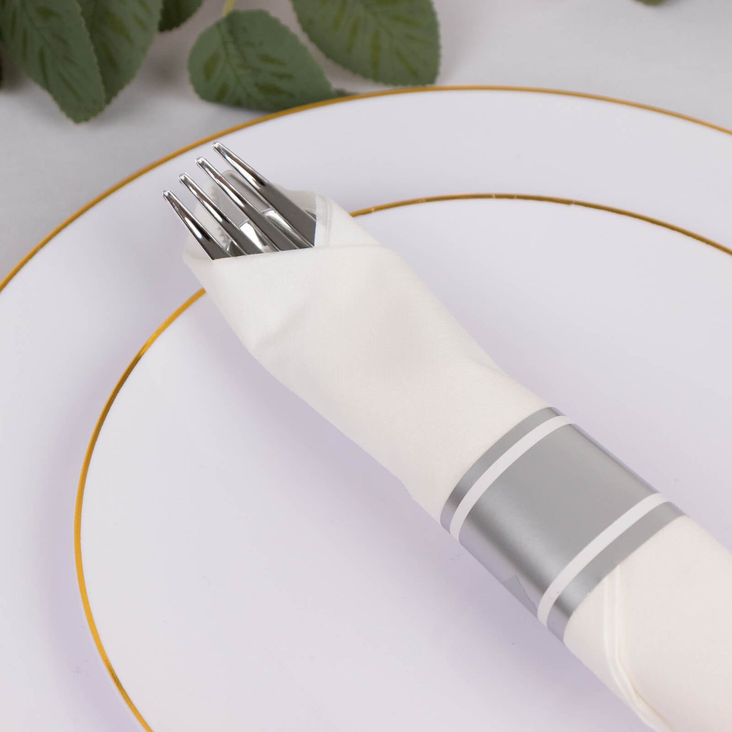 Silver disposable cutlery set with white napkin on a plate.