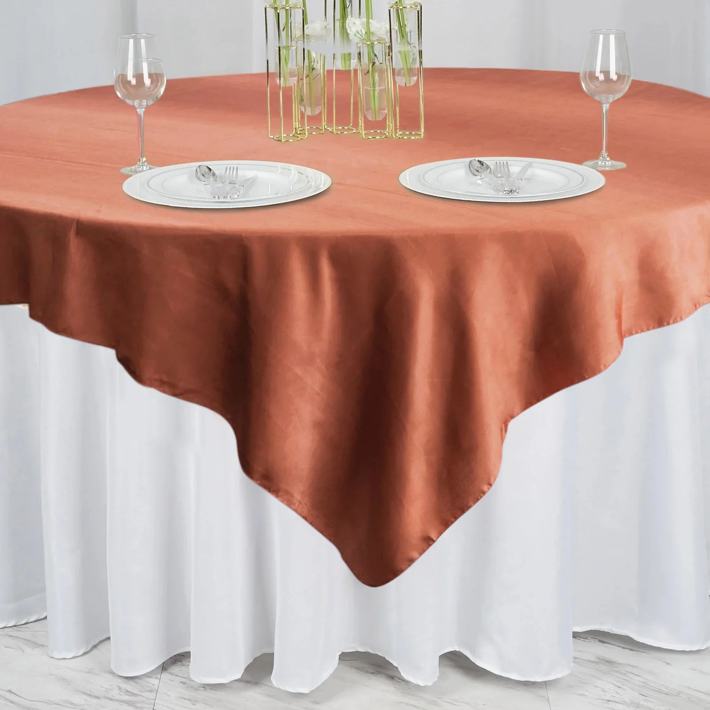 Terracotta satin square tablecloth overlay on a round table setting.