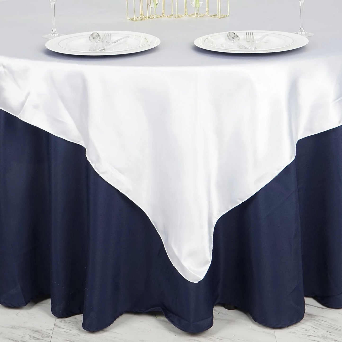 White satin square tablecloth overlay on a dark blue table setting.