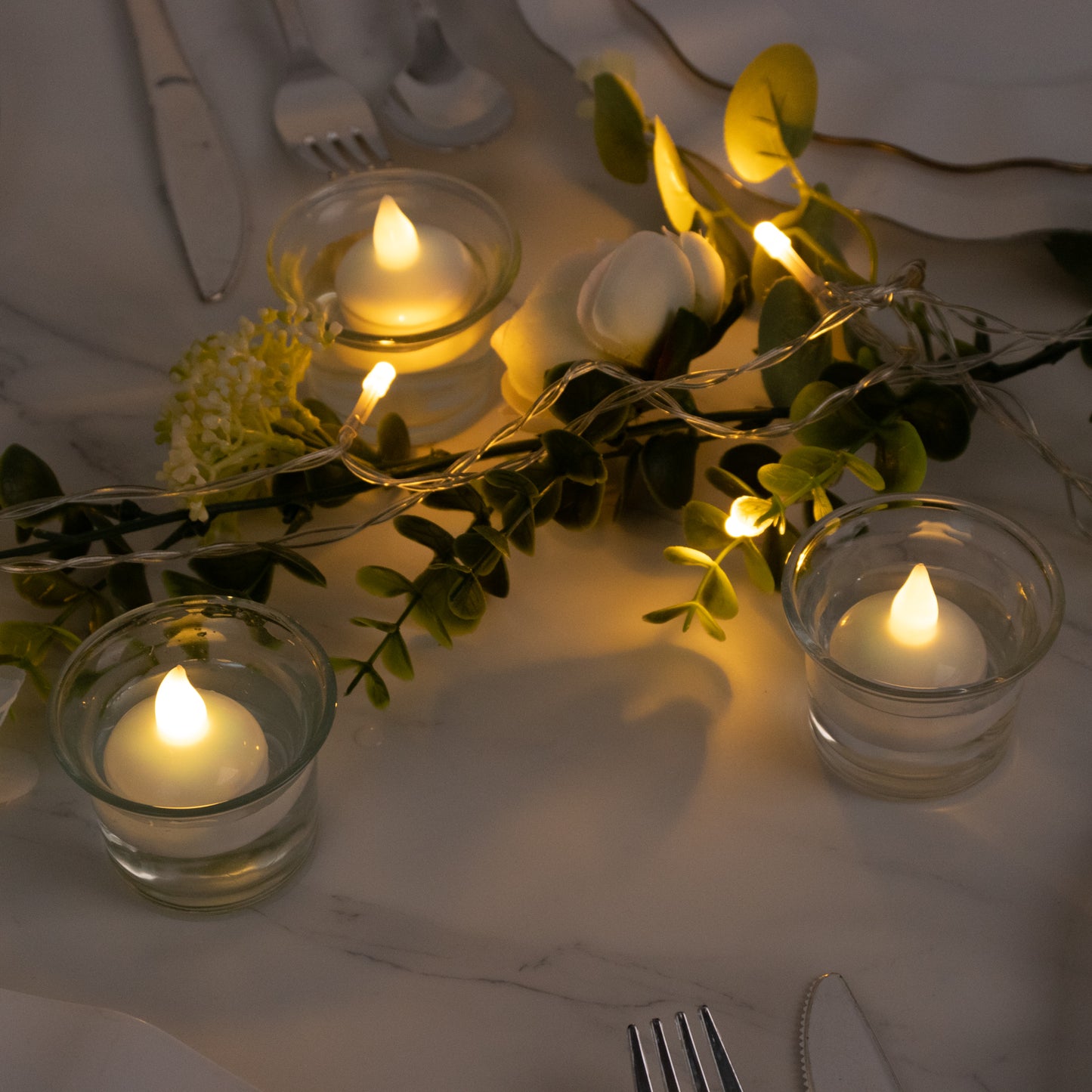 Warm white flameless tealight candles in glass holders on a table.