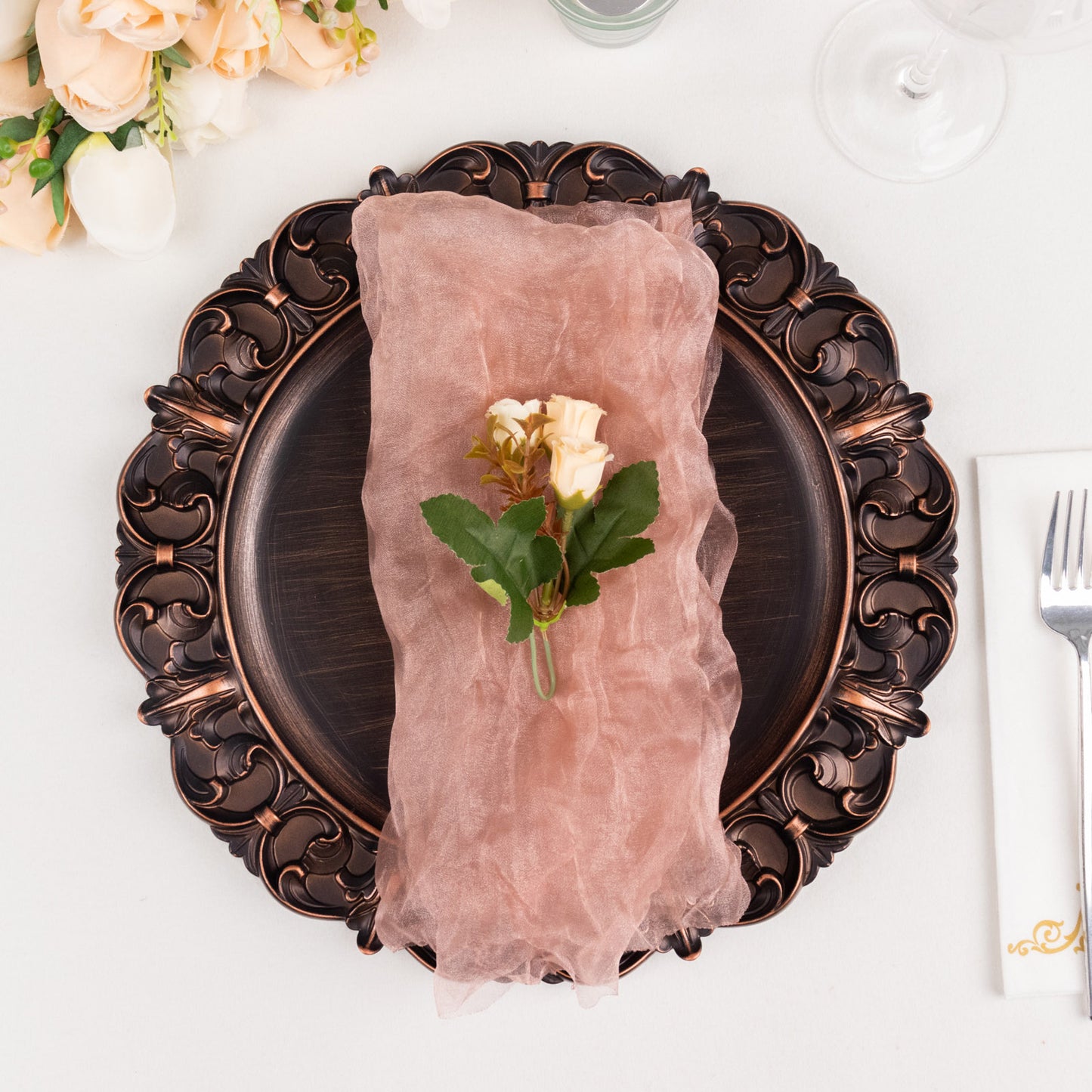 Dusty rose sheer crinkled organza dinner napkin on a decorative plate.