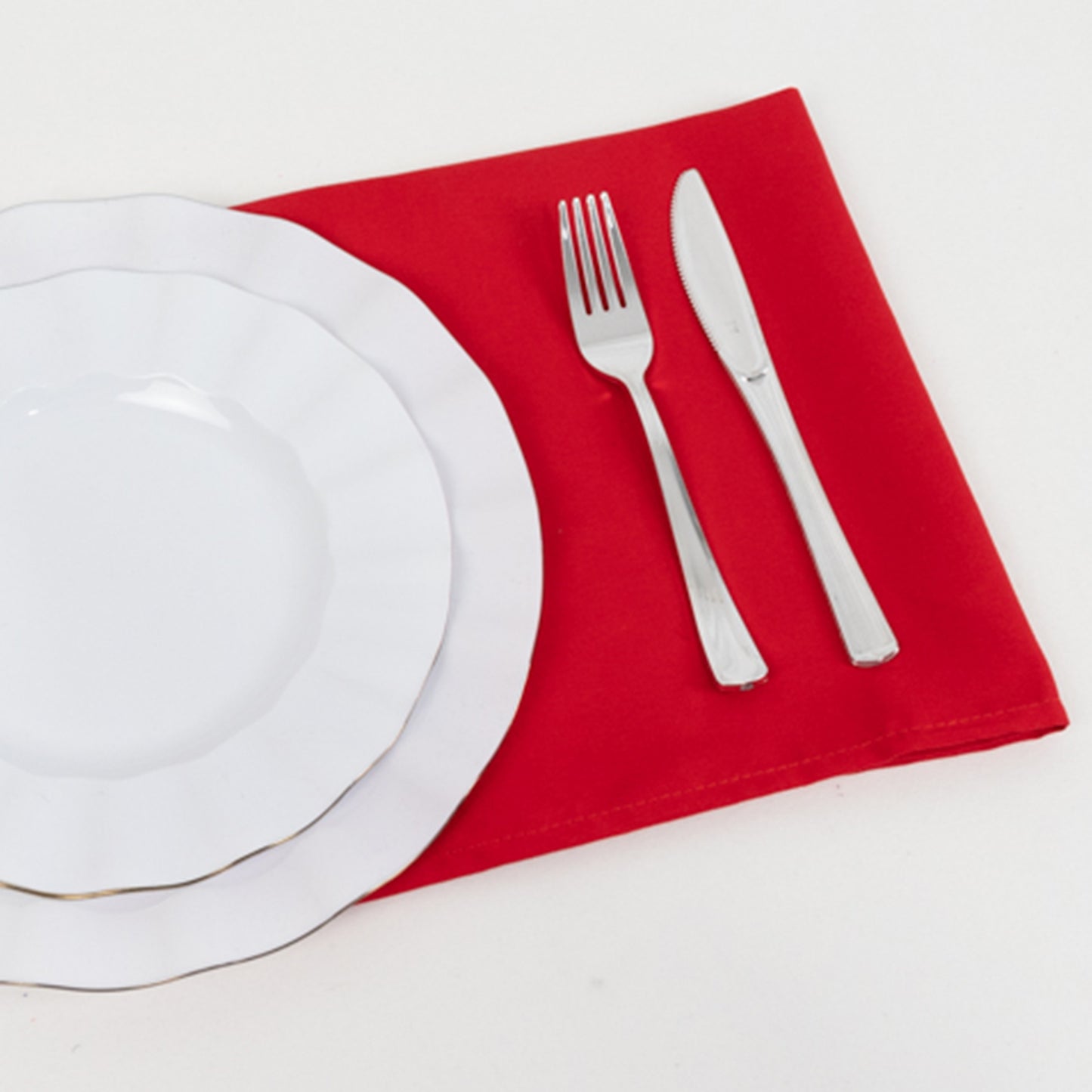 Red cotton blend cloth napkin with white dinnerware and silver utensils.