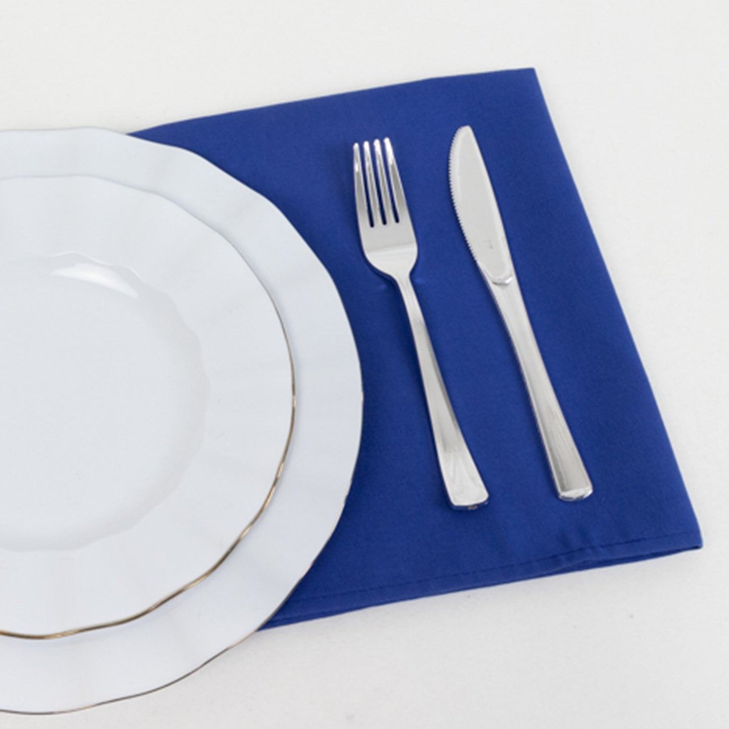 Royal blue cotton blend napkin under white dinner plate and silverware.