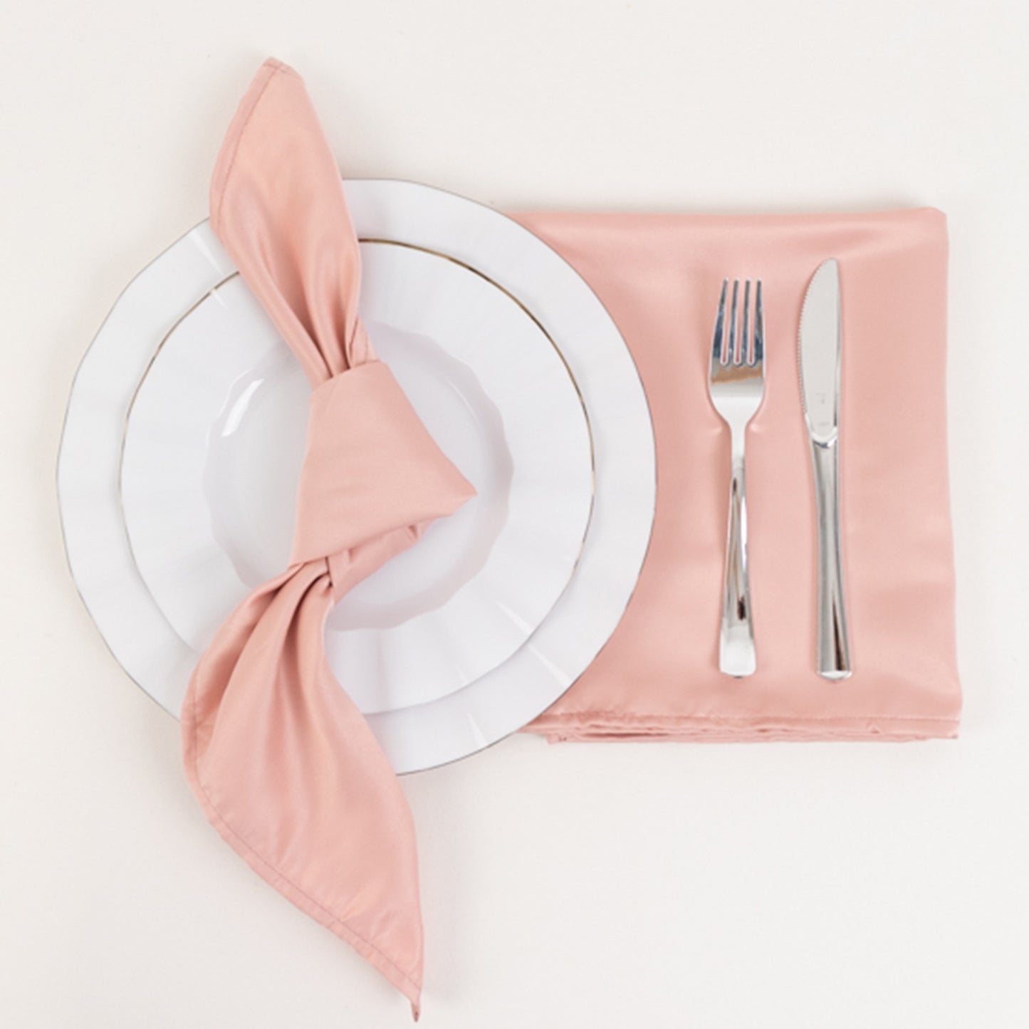 Dusty rose satin napkins arranged with a plate and cutlery.