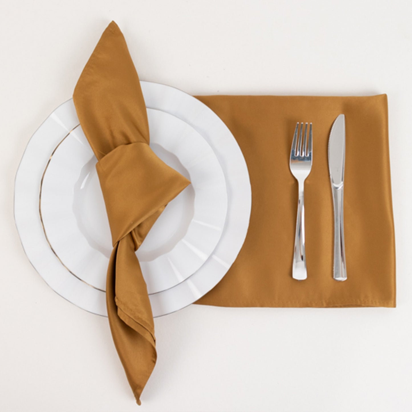 Gold satin napkin on a white plate with cutlery.