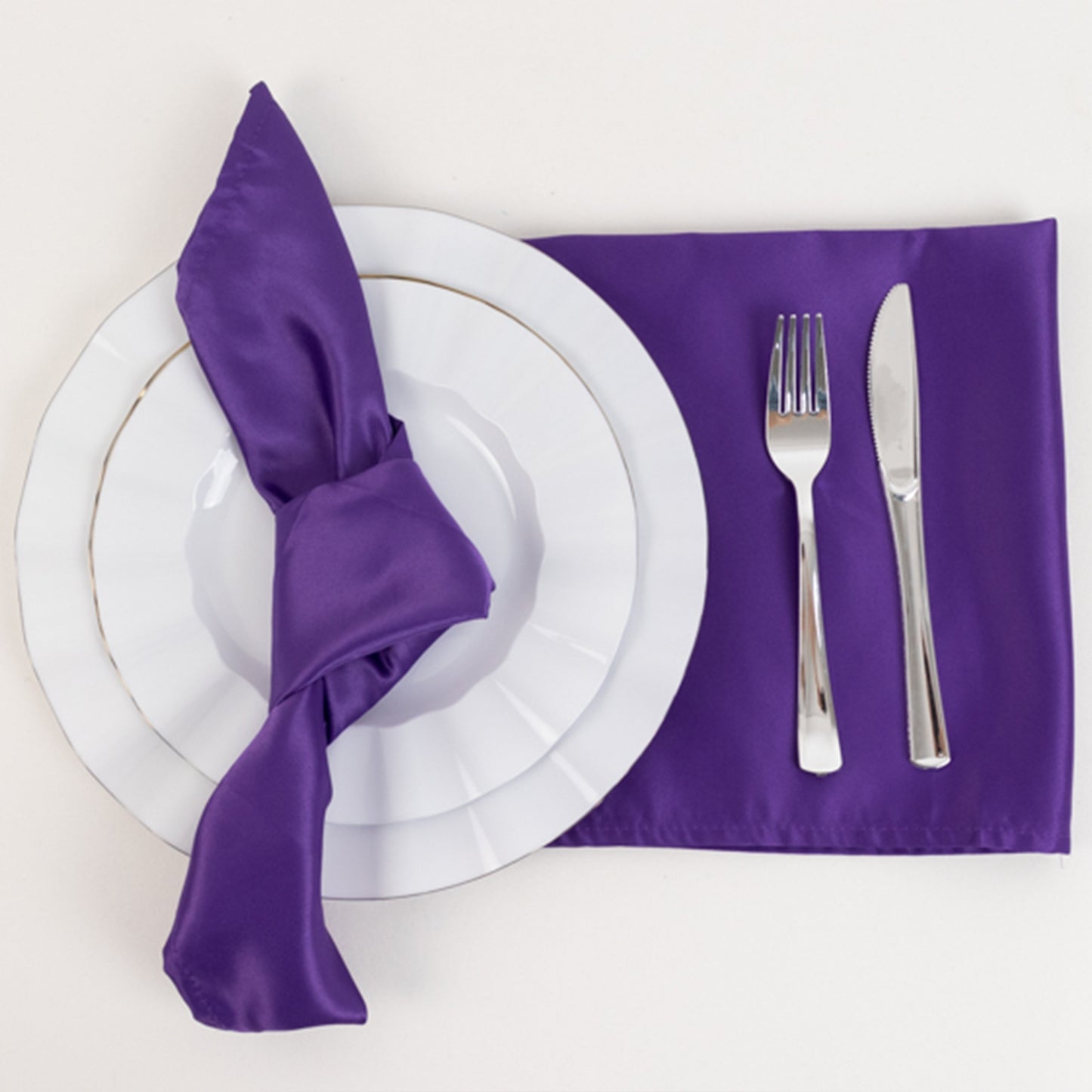 Purple satin napkins on a table setting with white plates and silver cutlery.