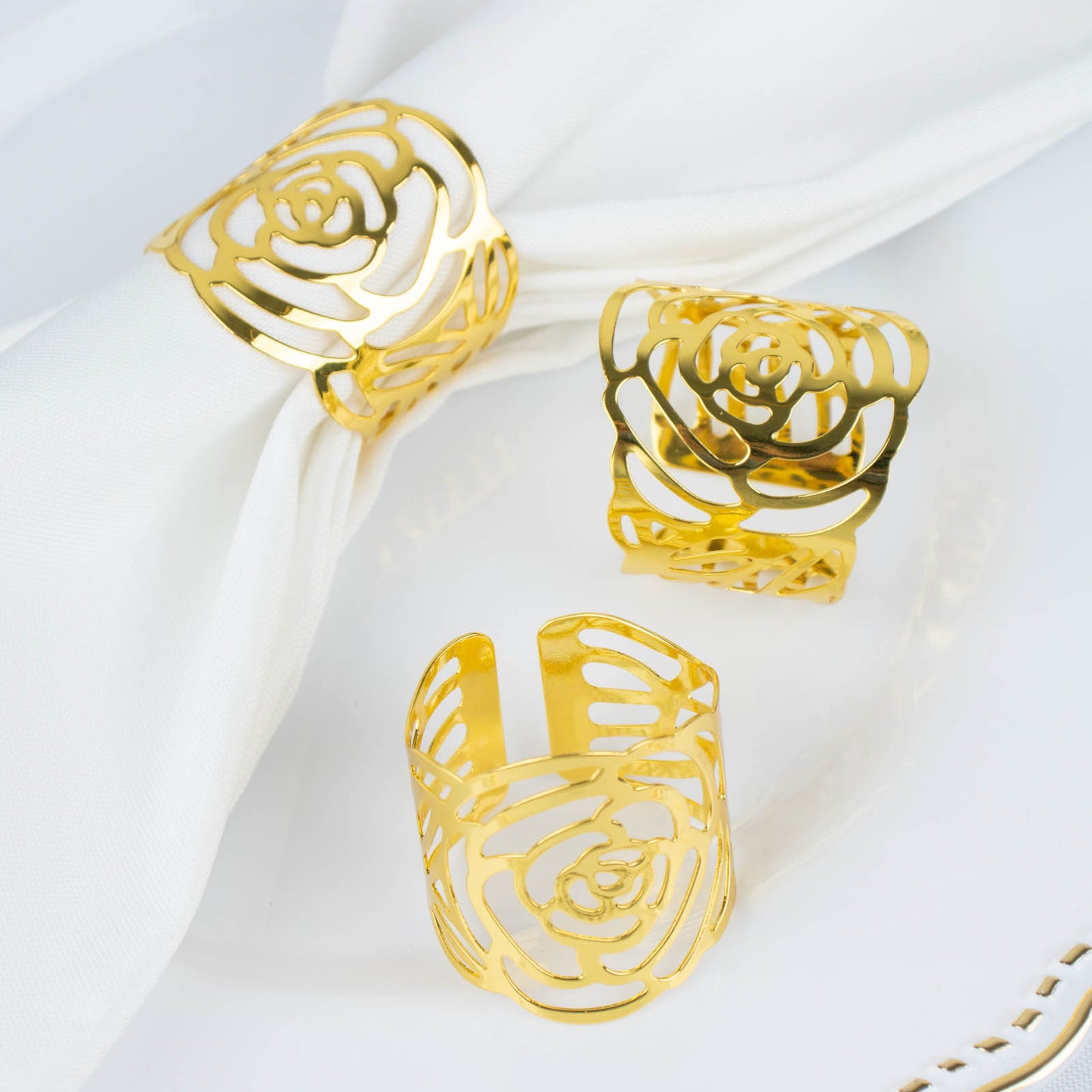 Shiny gold laser cut rose round metal napkin rings on a white napkin.