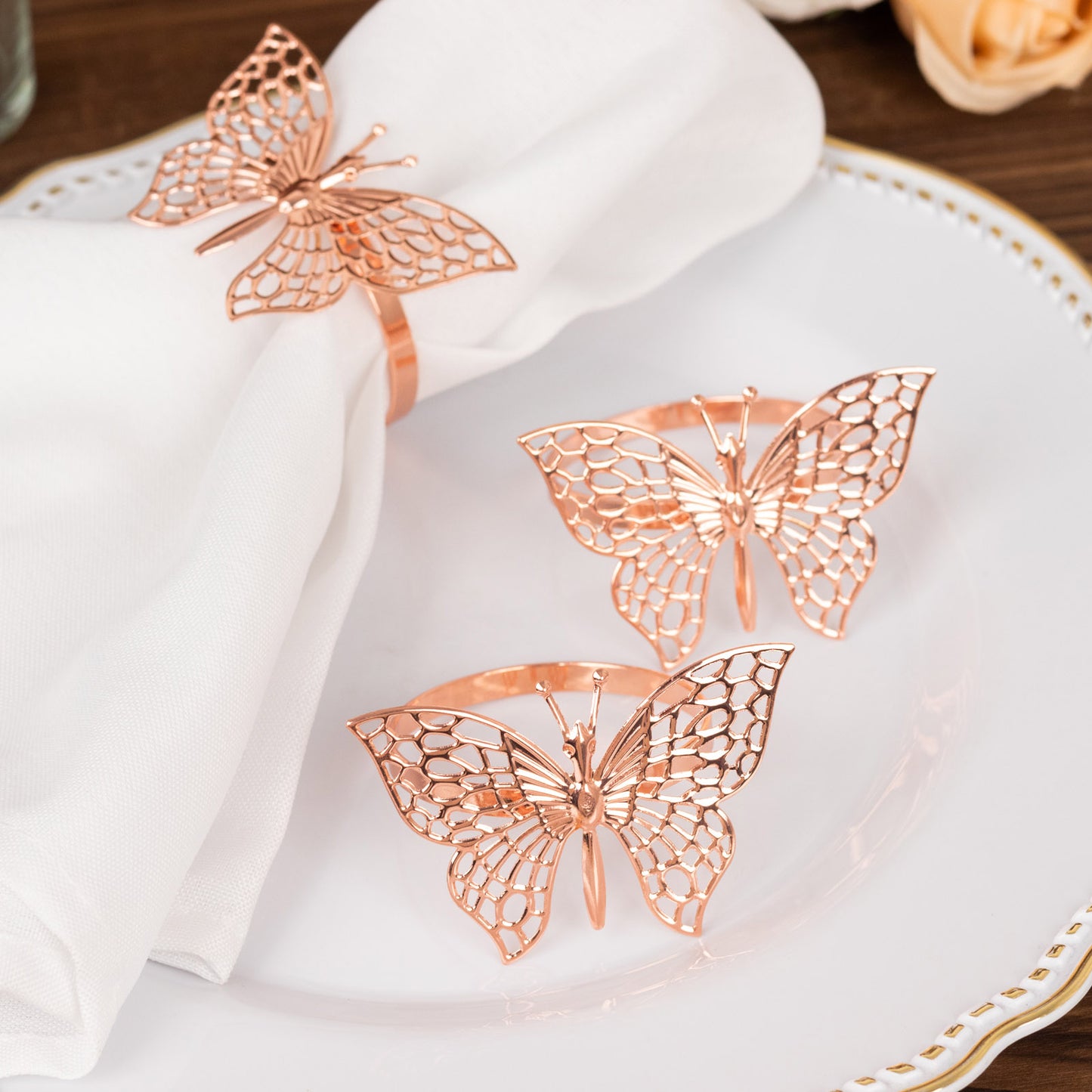 Rose gold metal butterfly napkin rings on a white plate with cloth napkins.