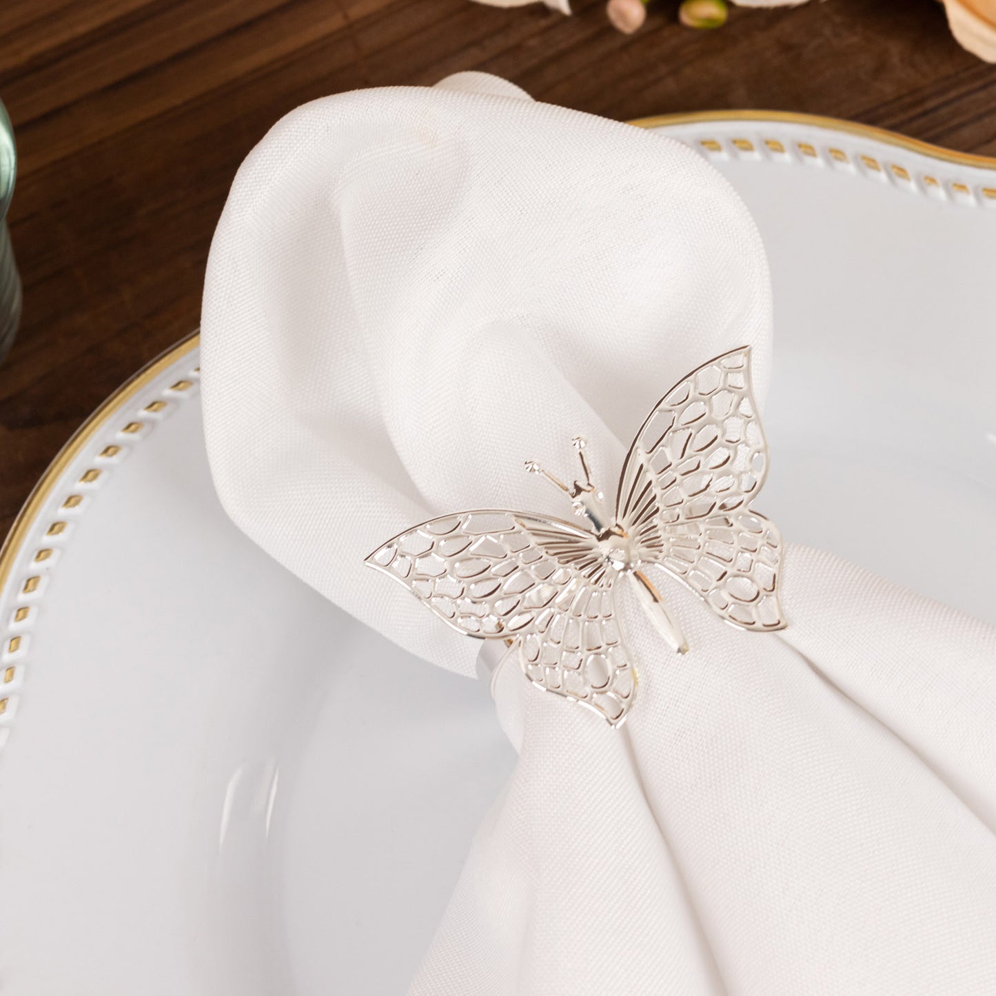 Silver metal butterfly napkin ring on a white cloth napkin.