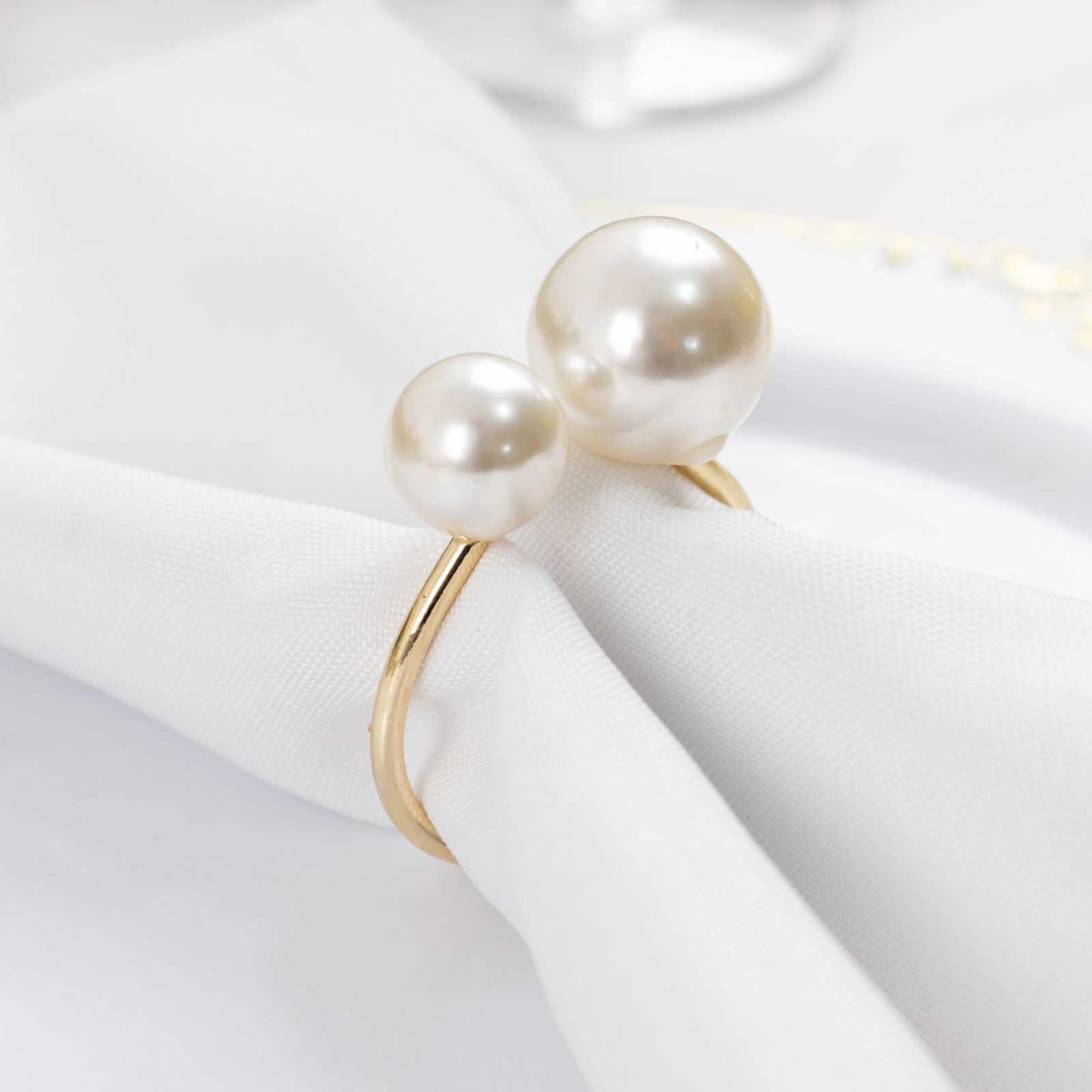 White pearl and gold metal napkin holder on a white napkin.