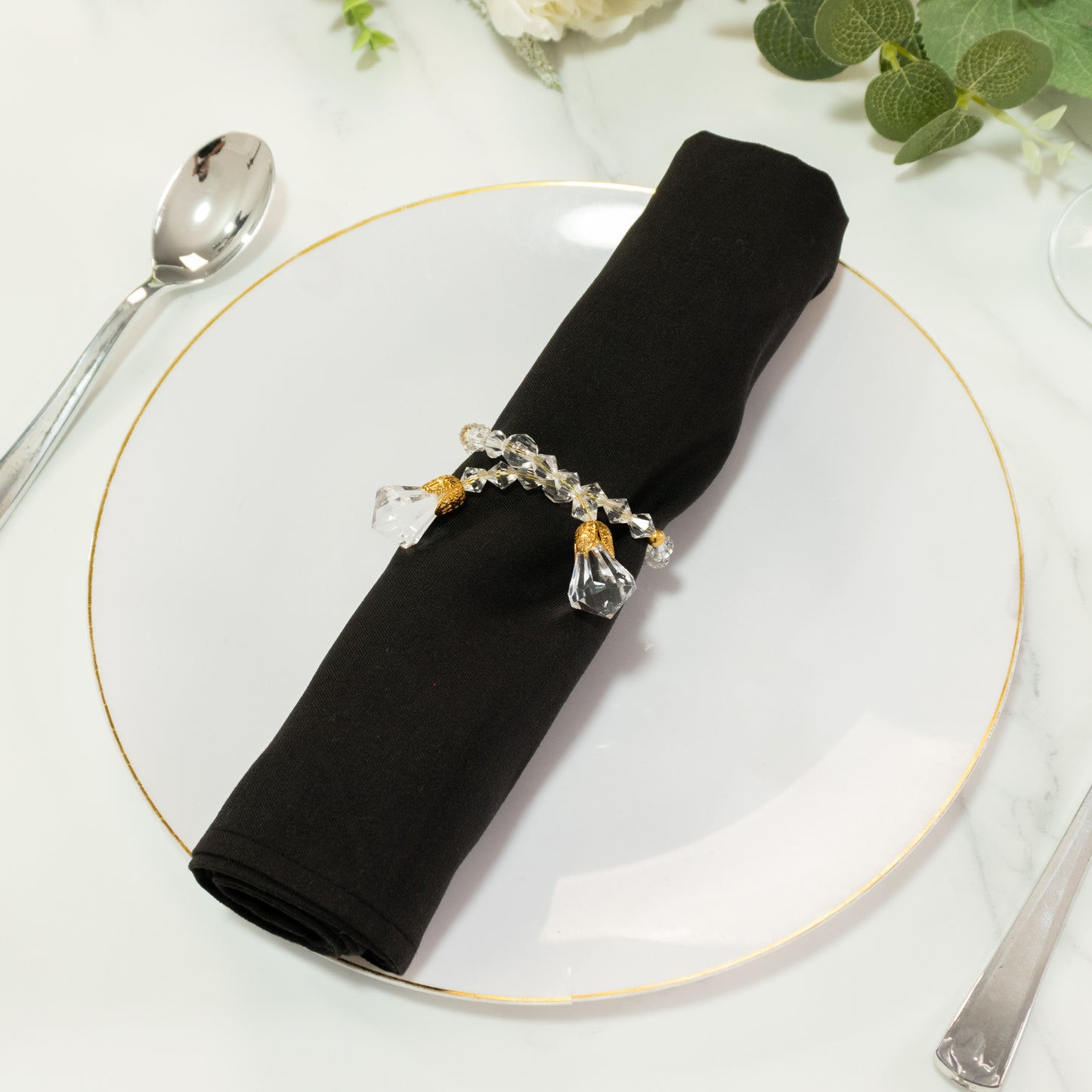 Clear crystal beaded napkin ring with gold accents on a black napkin.