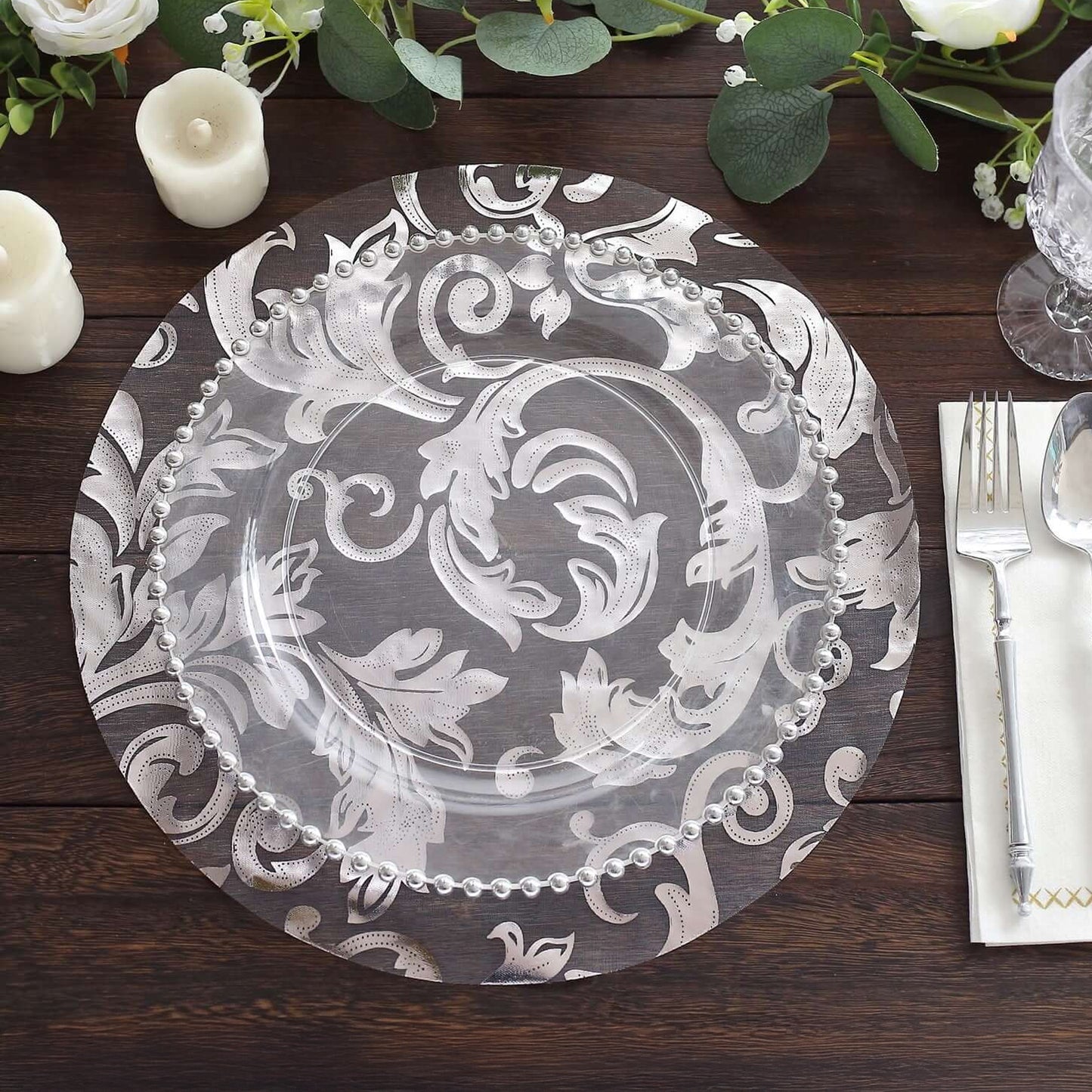 Metallic silver round placemat with floral design on a wooden table.
