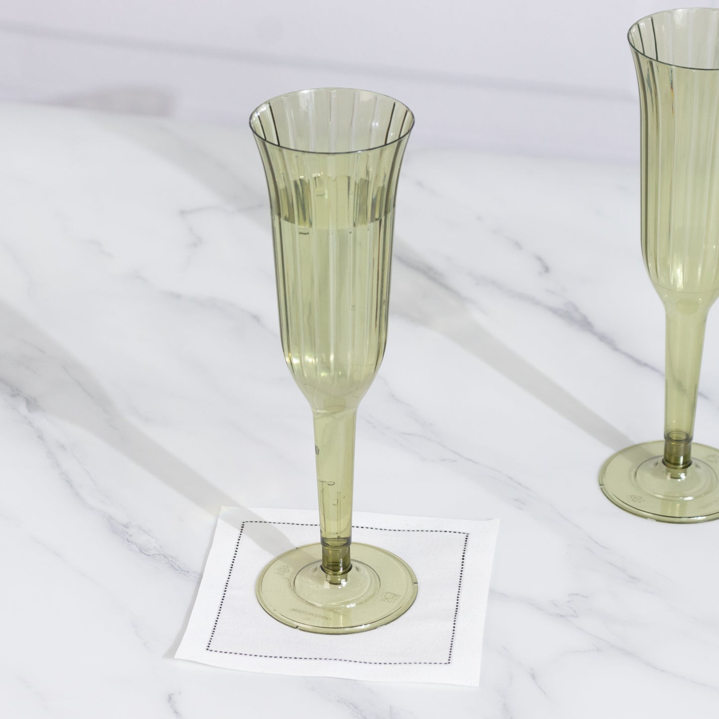 Dusty sage green plastic champagne flute on a marble surface.