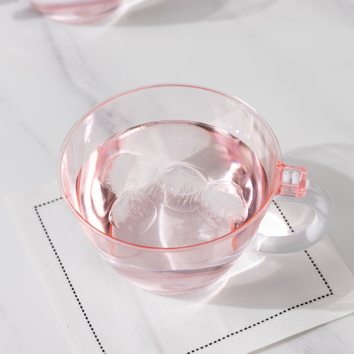 Transparent blush coffee cup with handle filled with water and ice.