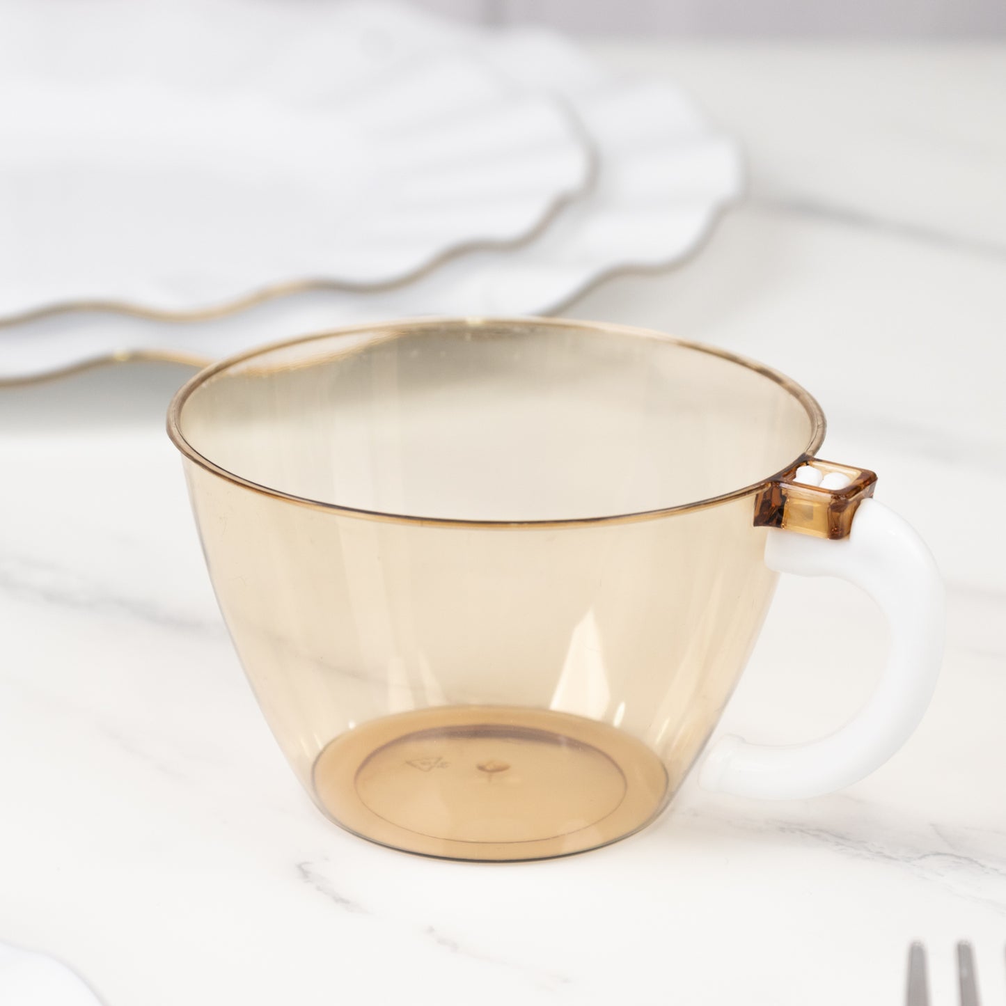Amber gold disposable plastic coffee cup with handle on a marble surface.