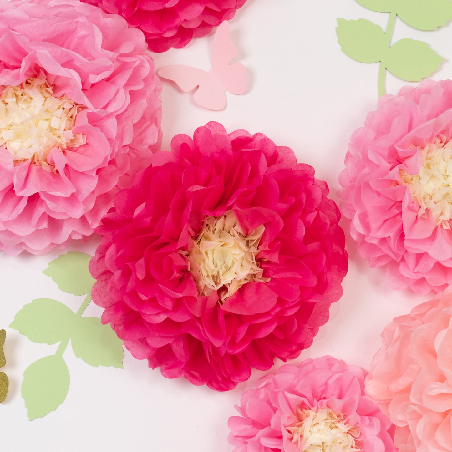 Blush pink tissue paper flowers pom poms with butterflies and olive leaves.