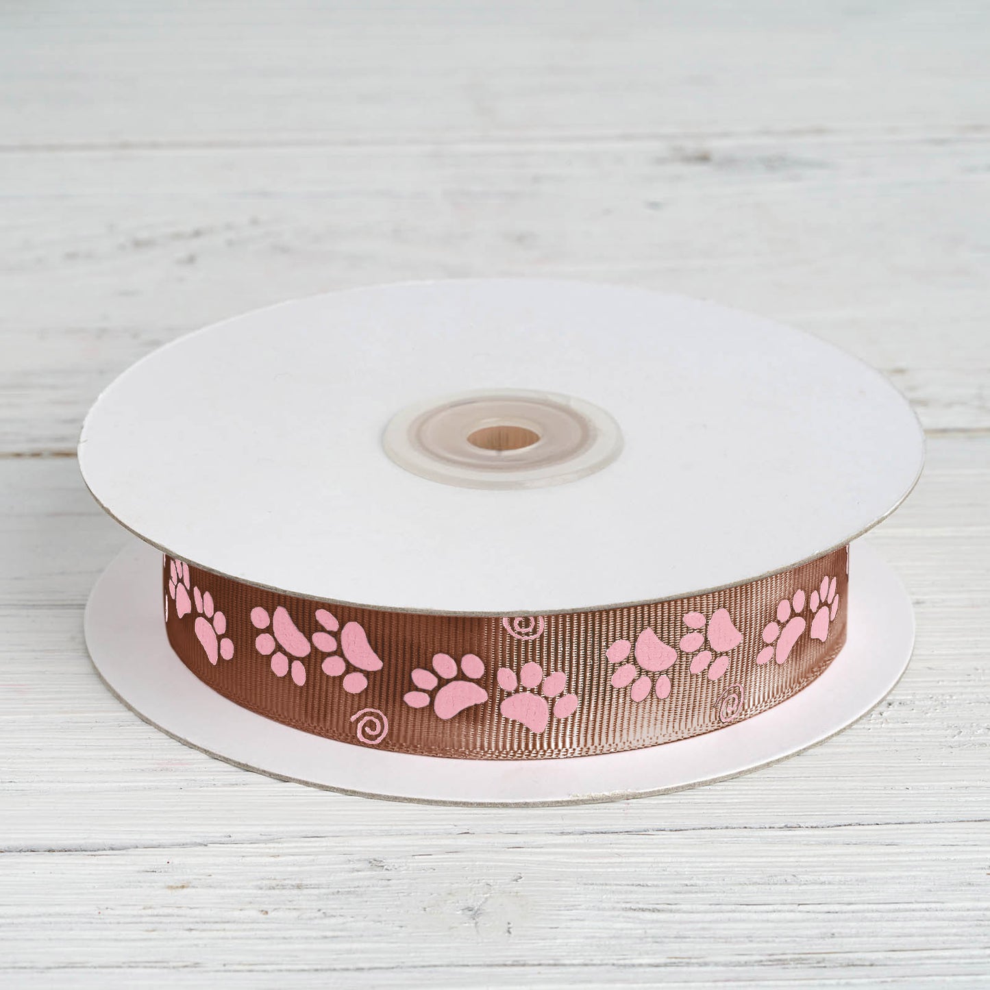 Chocolate brown and pink paw print satin ribbon on a spool.