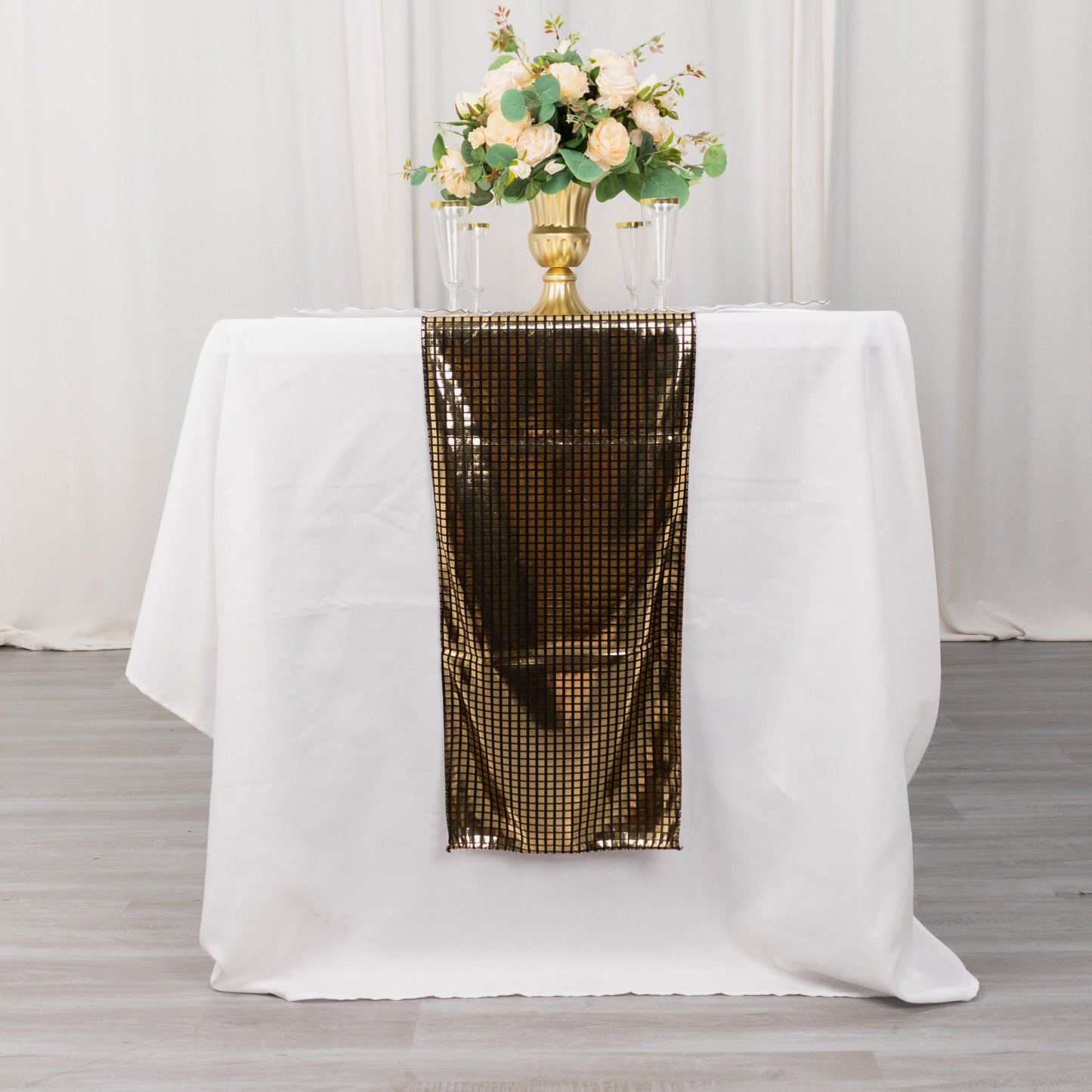 Shiny black gold foil table runner on a white table with flowers.
