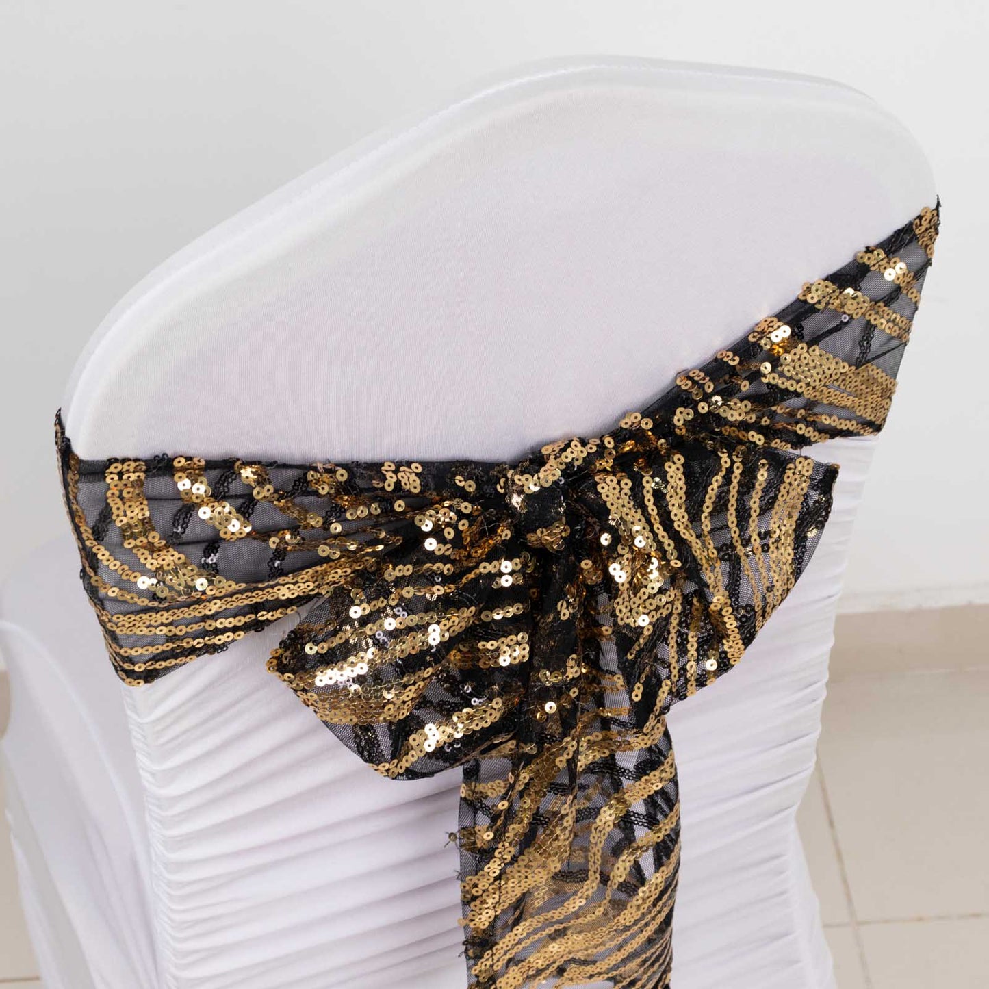 Black and gold wave embroidered sequin chair sash on a white chair.
