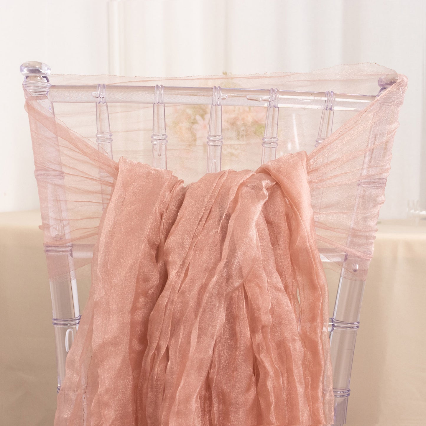 Dusty rose sheer crinkled organza chair sash on a transparent chair.