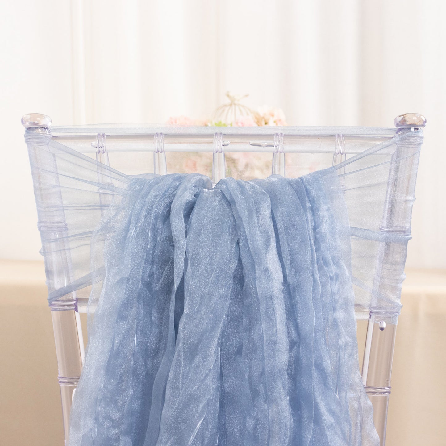 Dusty blue sheer crinkled organza chair sash on a transparent chair.