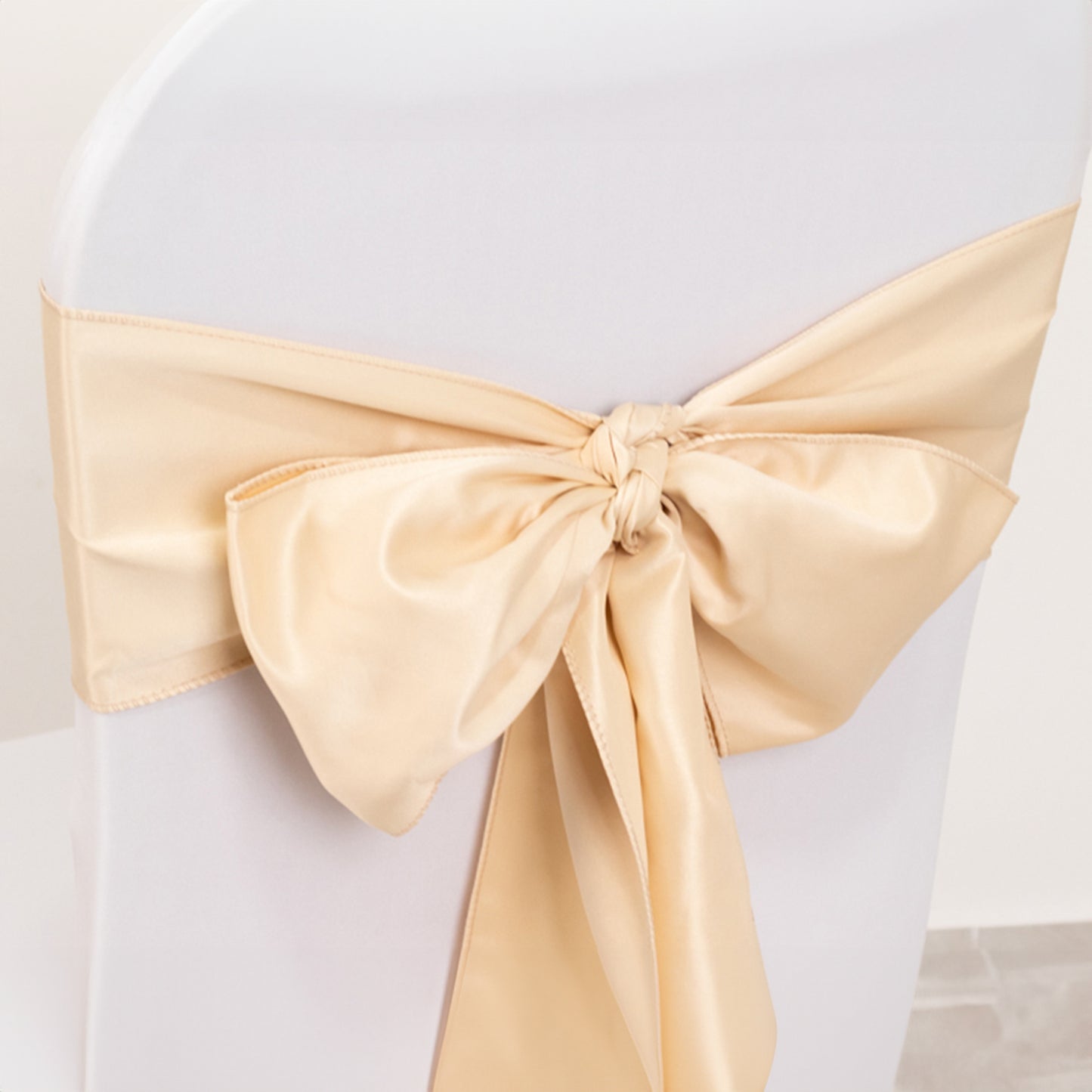 Beige satin chair sash and bow on a white chair.