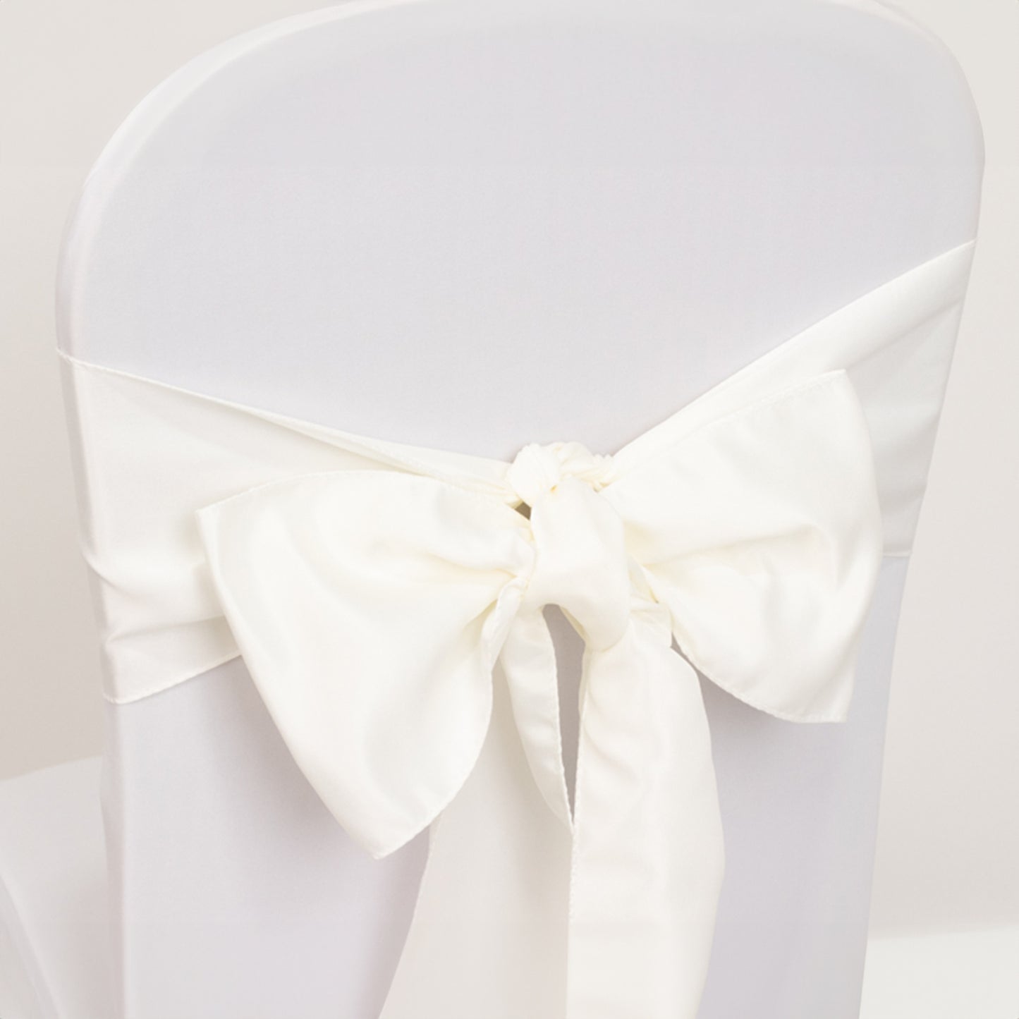Ivory satin chair sash bow on a white chair.