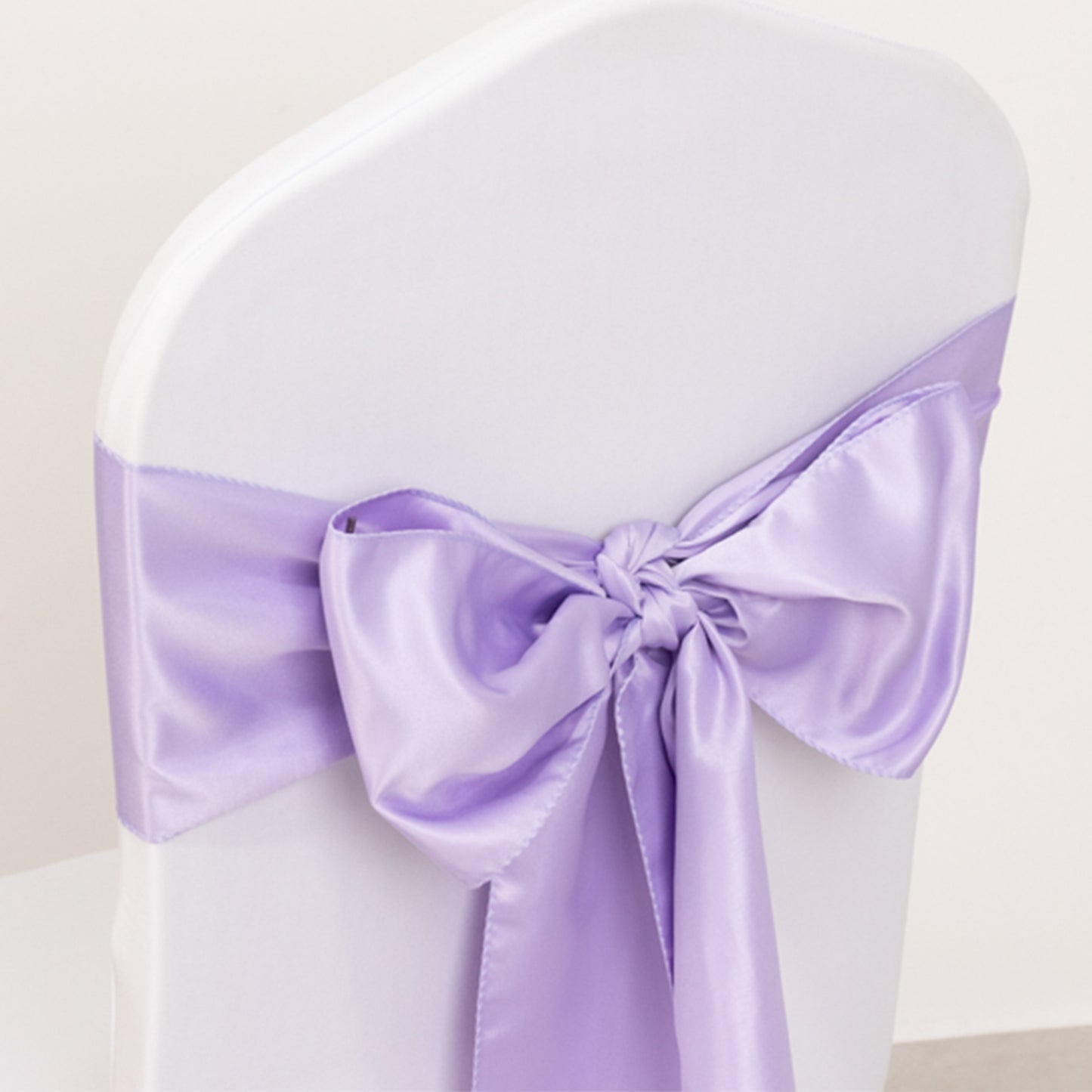 Lavender satin chair sash with bow on a white chair.