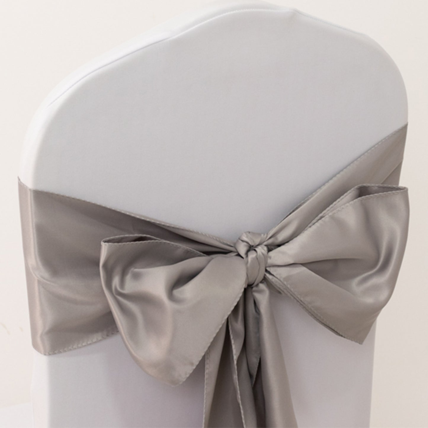 Silver satin chair sash tied in a bow on a white chair.