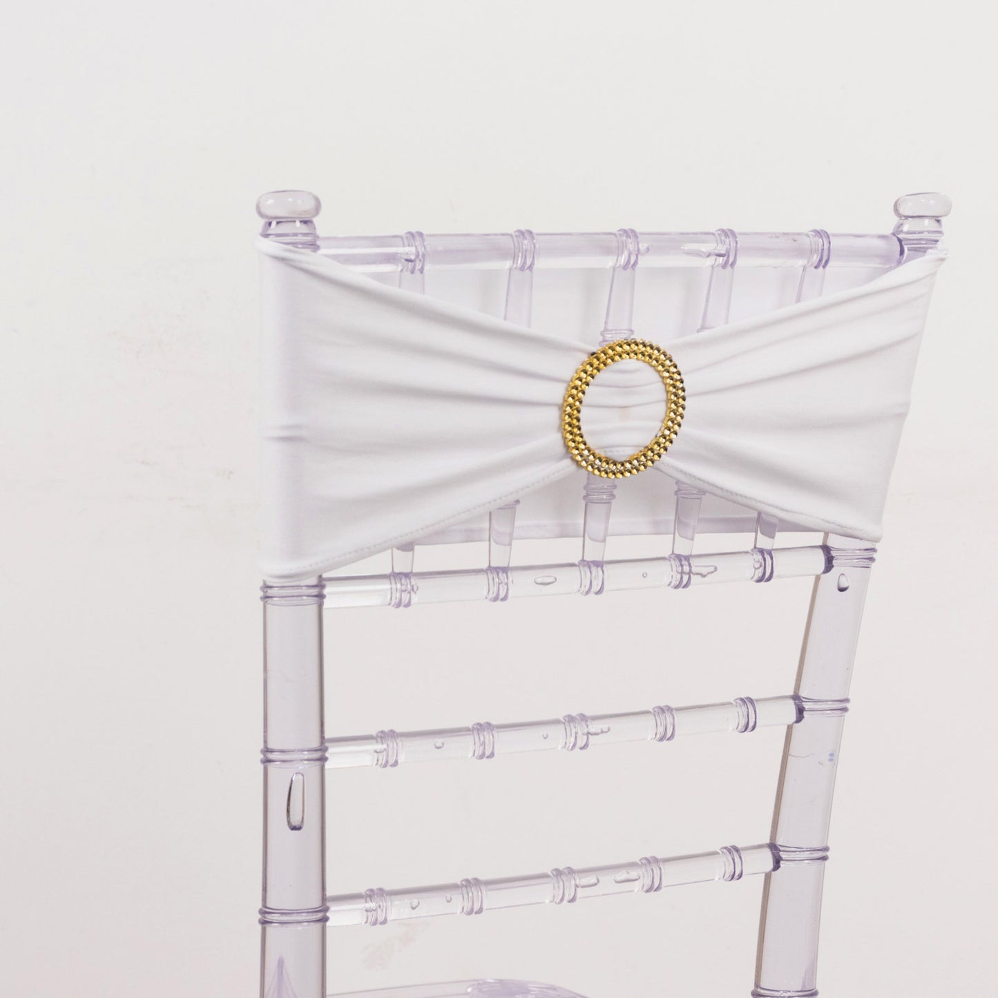 White spandex chair sash with gold diamond buckle on a clear chair.