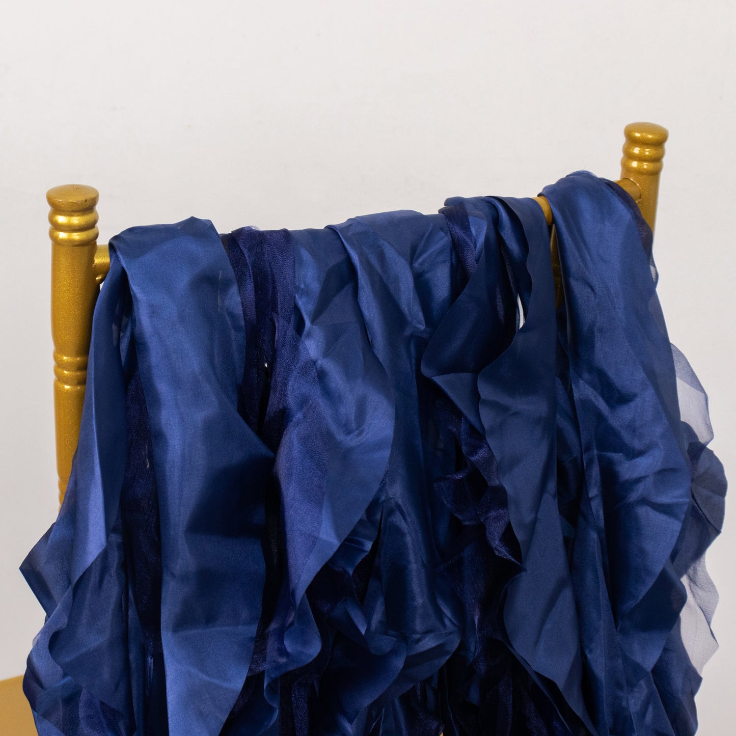 Navy blue curly chiffon satin chair sashes draped on a gold chair.