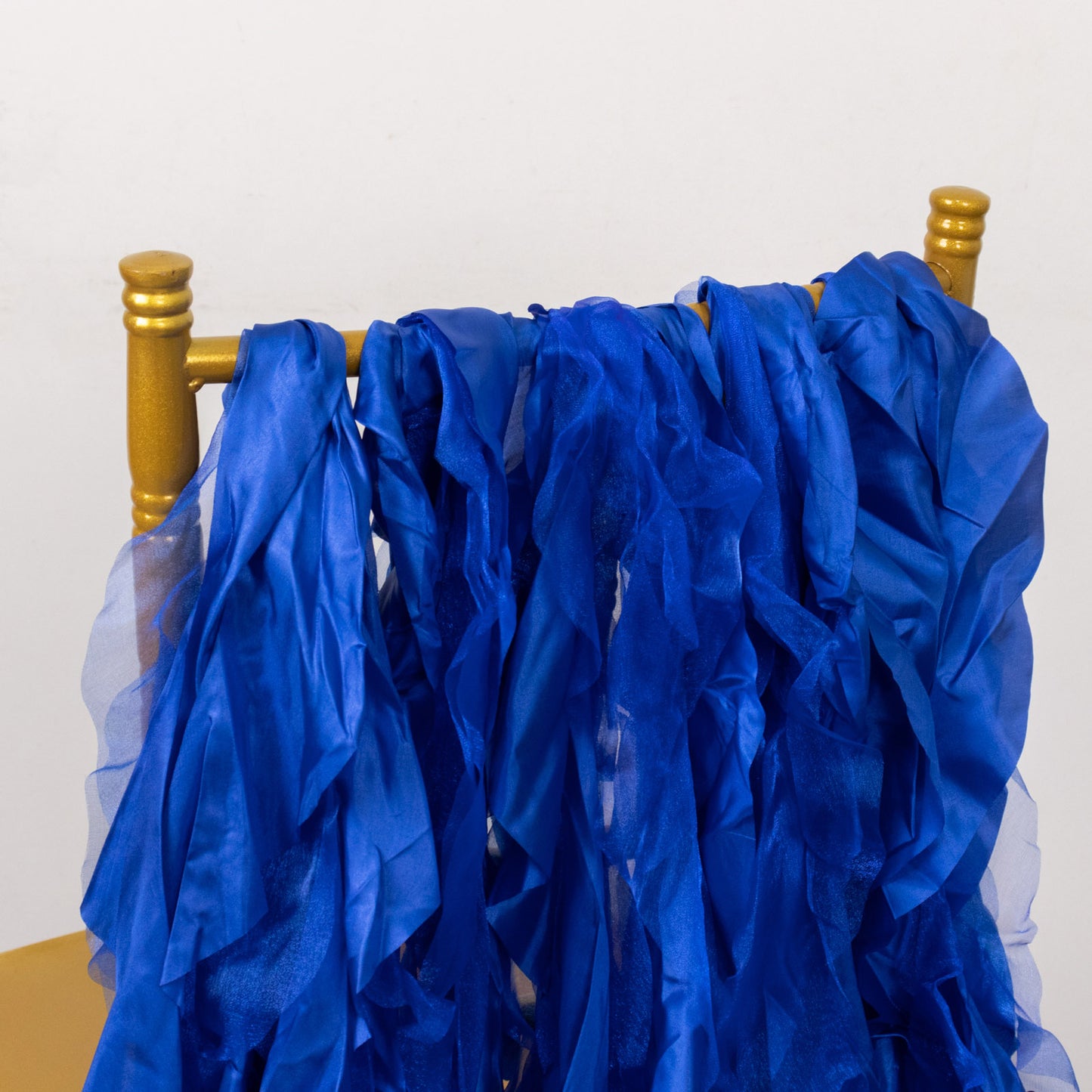 Royal blue curly chiffon satin chair sashes hanging on a gold chair.