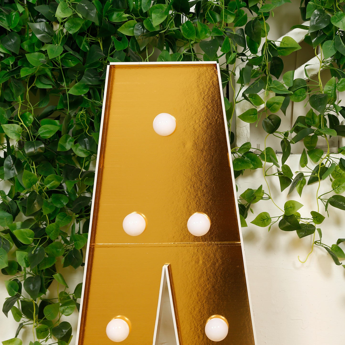 Gold LED marquee letter "A" with warm white lights against a green backdrop.